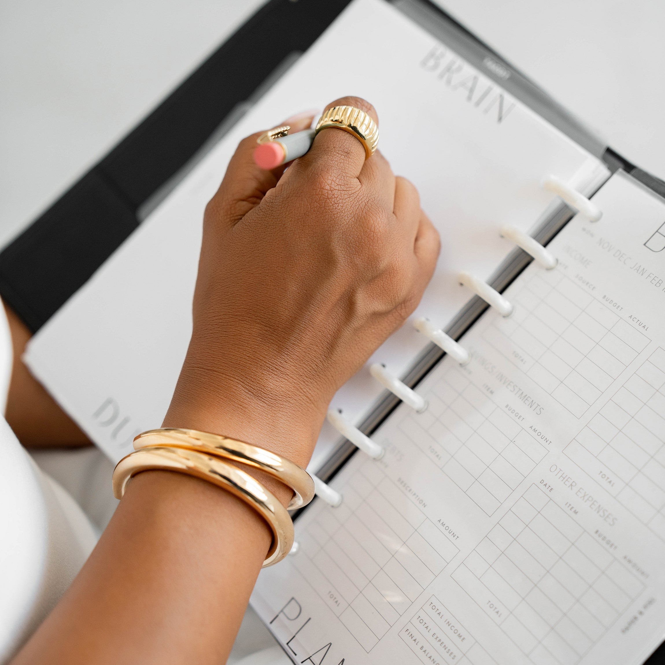 Close-up of a hand wearing gold bracelets writing in a planner