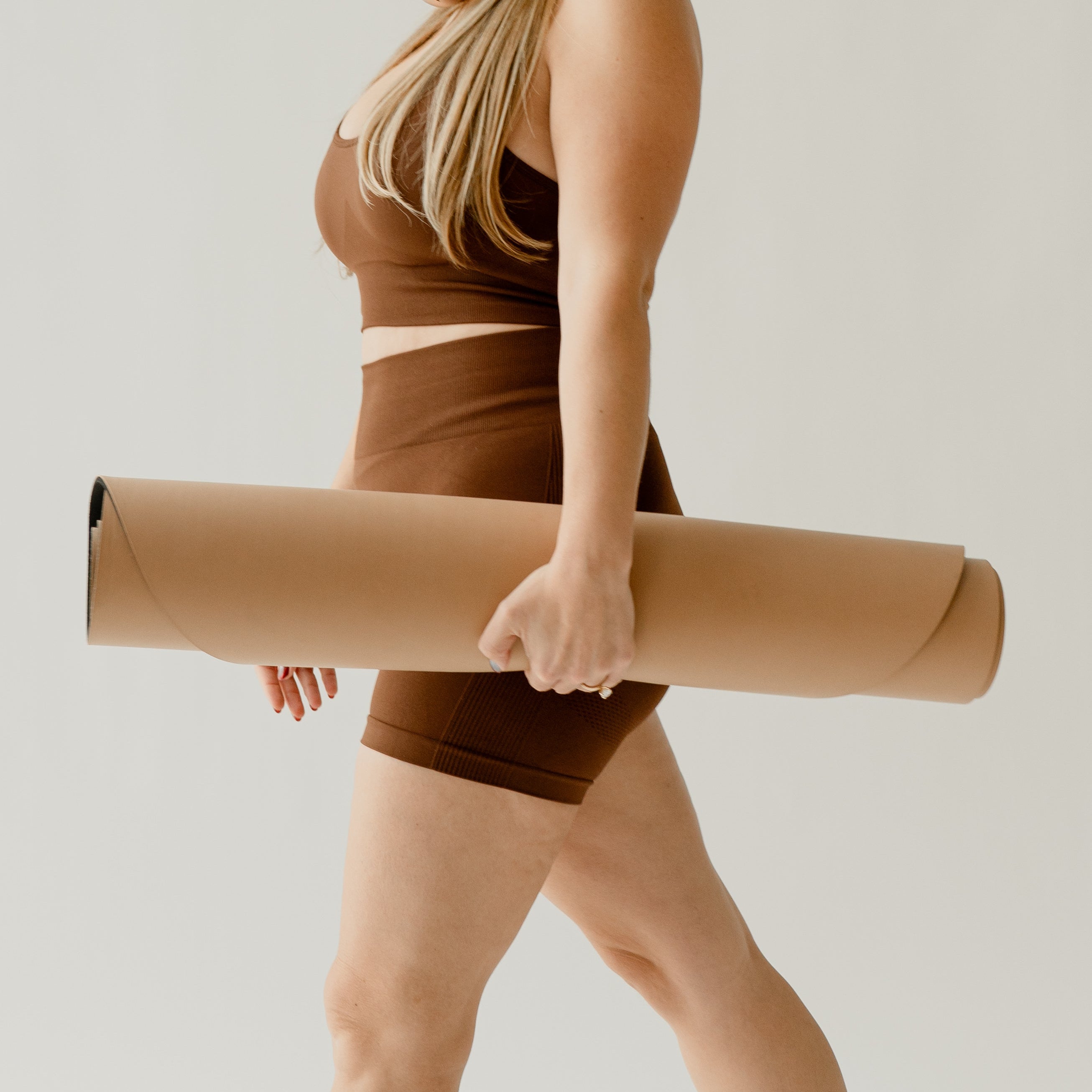 Woman walking with a yoga mat, wearing wireless headphones