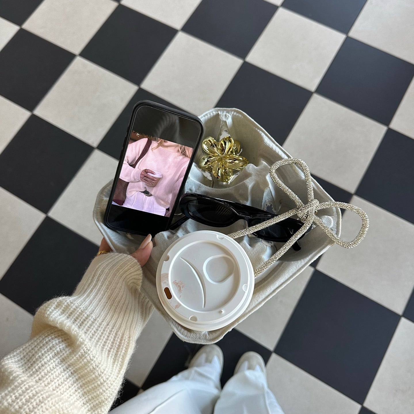 Overhead view of a person sitting on a checkered floor with a phone, a coffee and headphones