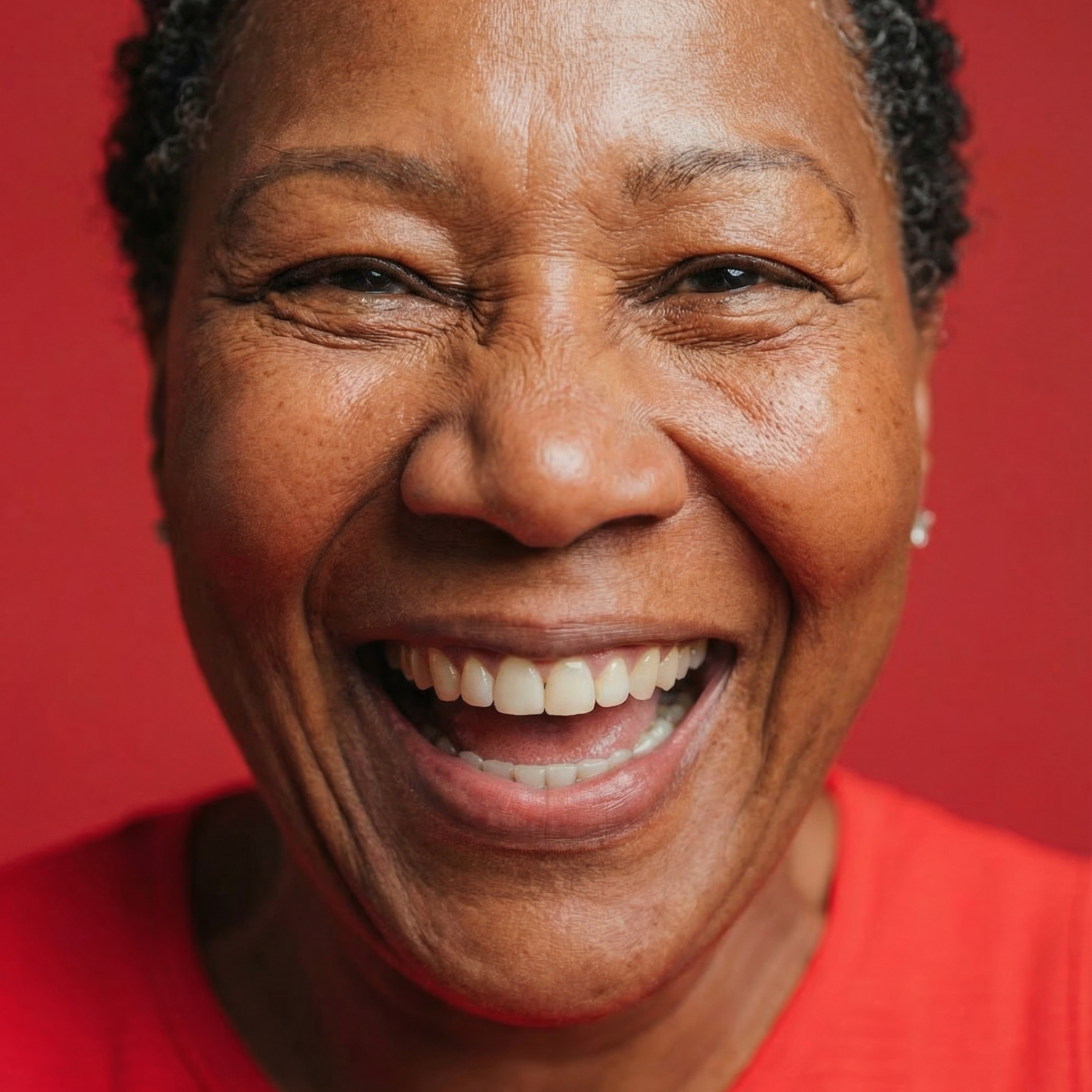Close-up portrait of a smiling woman with short gray hair wearing a red top