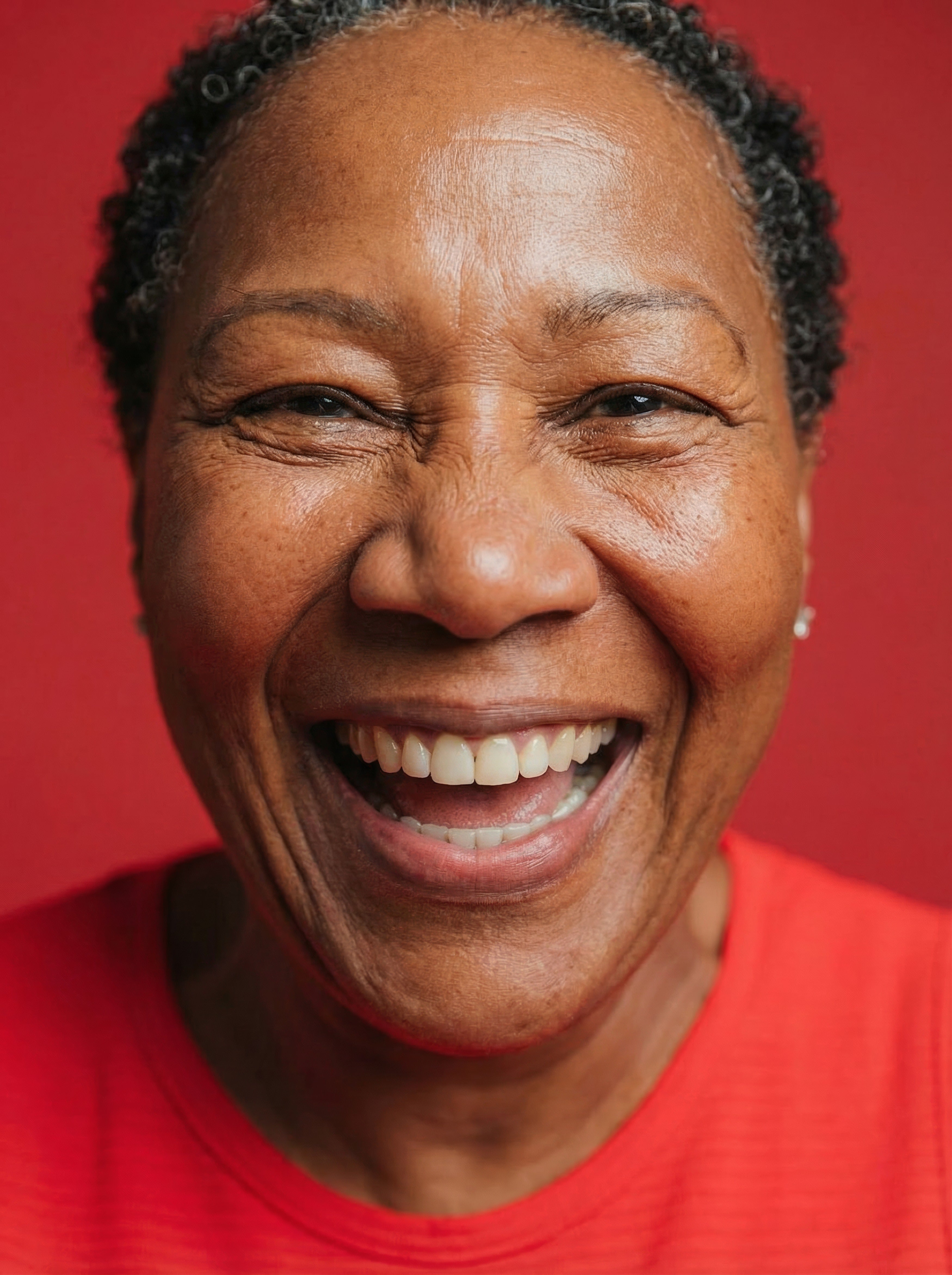 Close-up portrait of a smiling woman with short gray hair wearing a red top