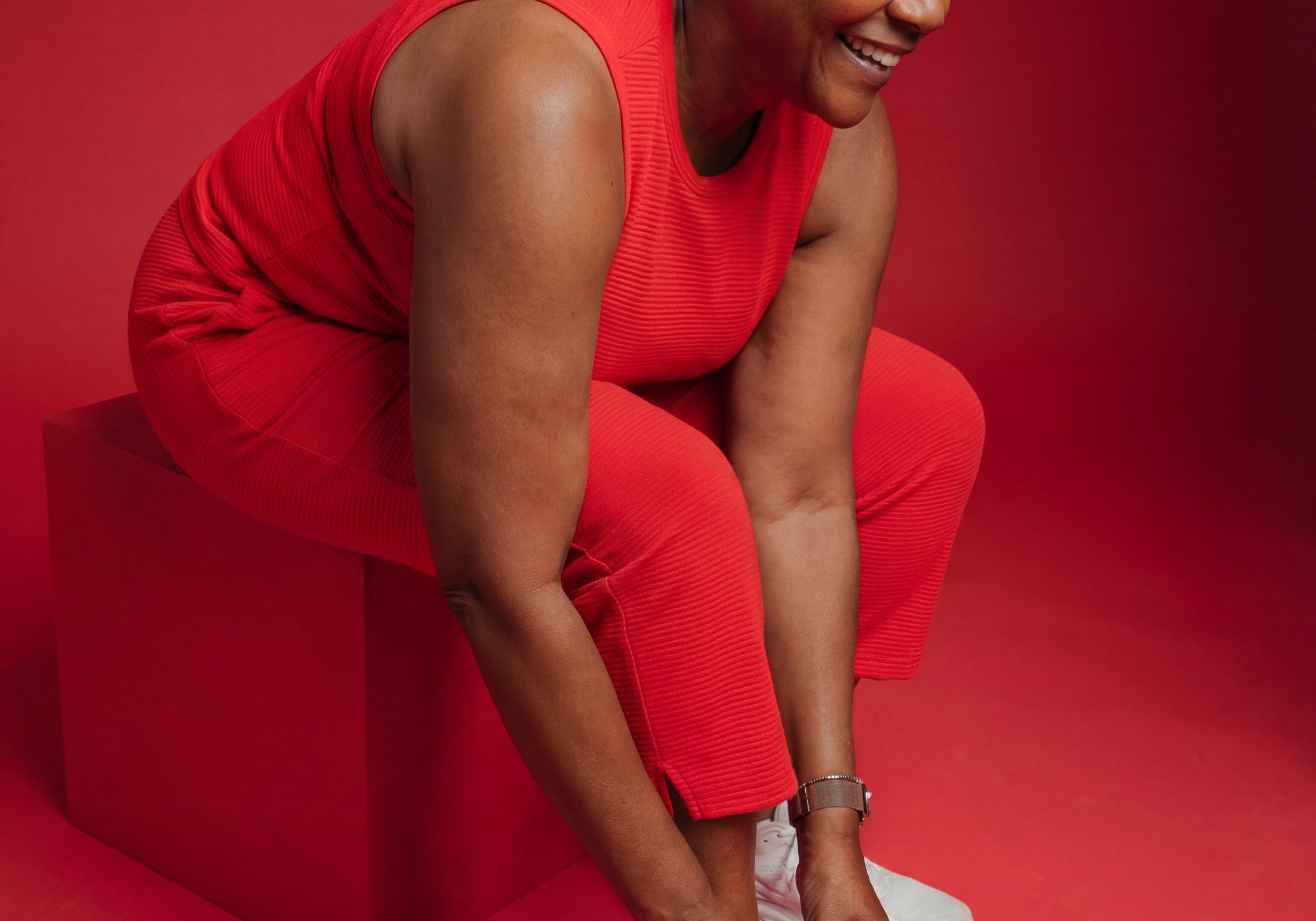 Woman in a red outfit tying her white sneakers against a bold red background