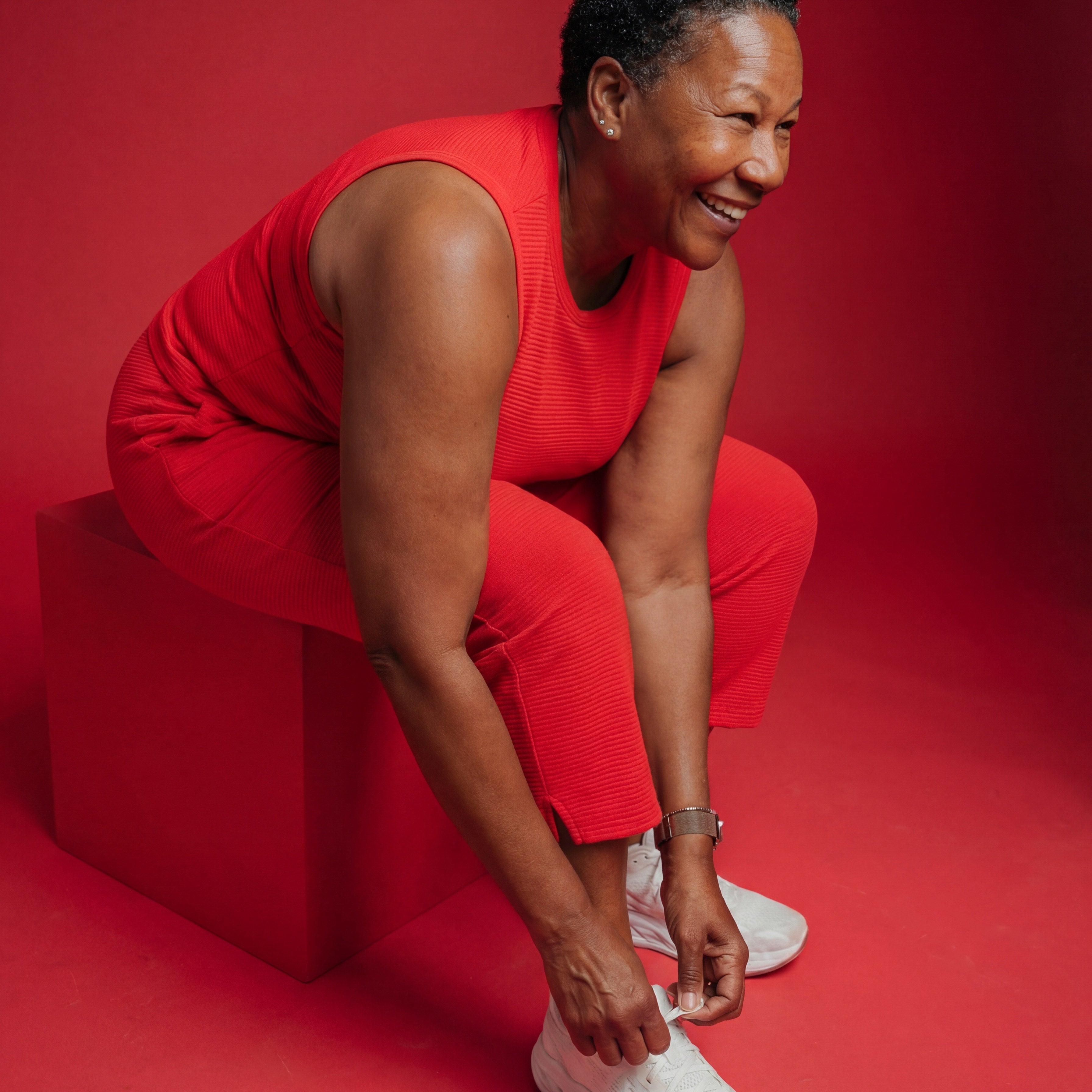 Woman in a red outfit tying her white sneakers against a bold red background