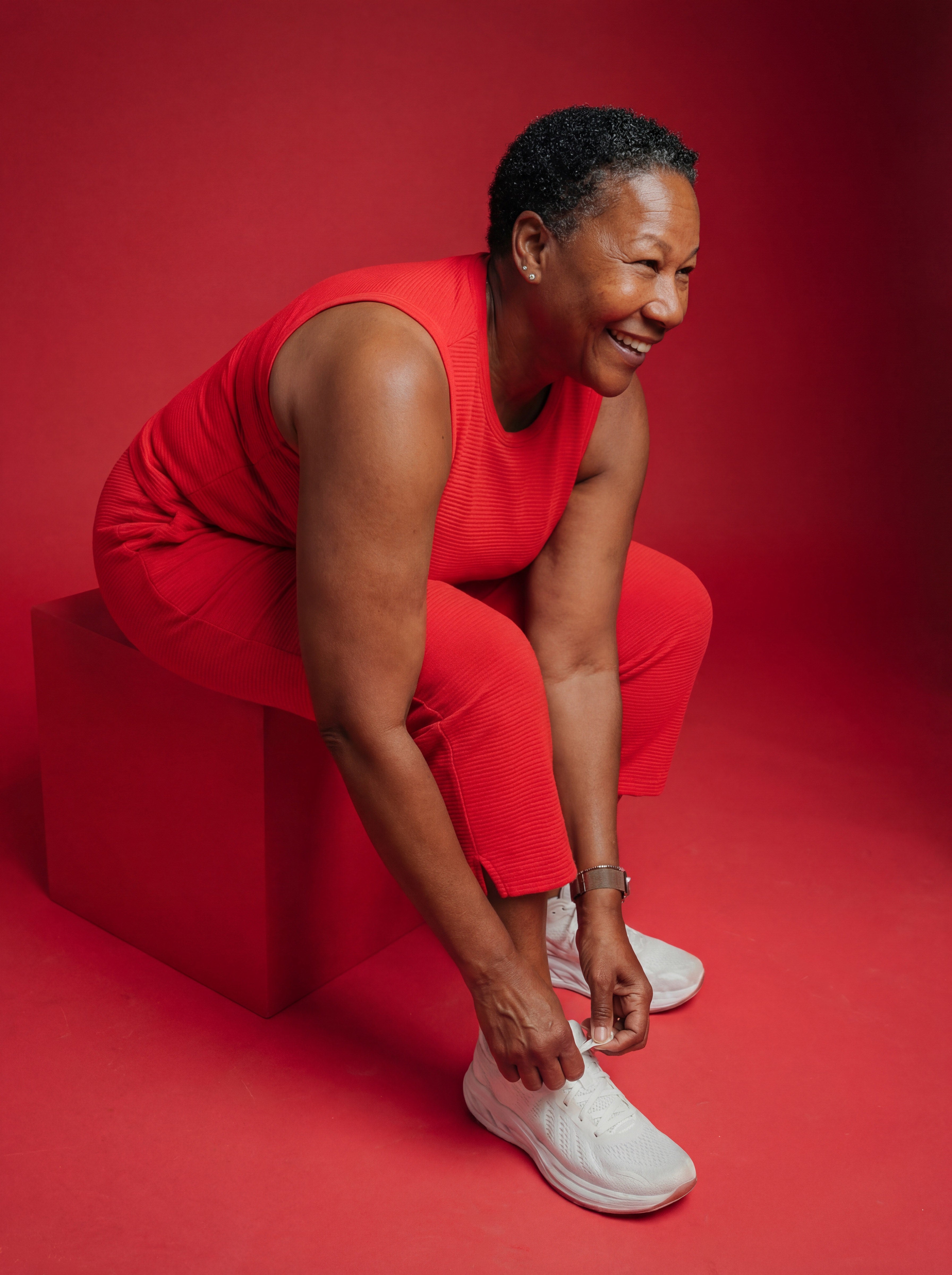 Woman in a red outfit tying her white sneakers against a bold red background