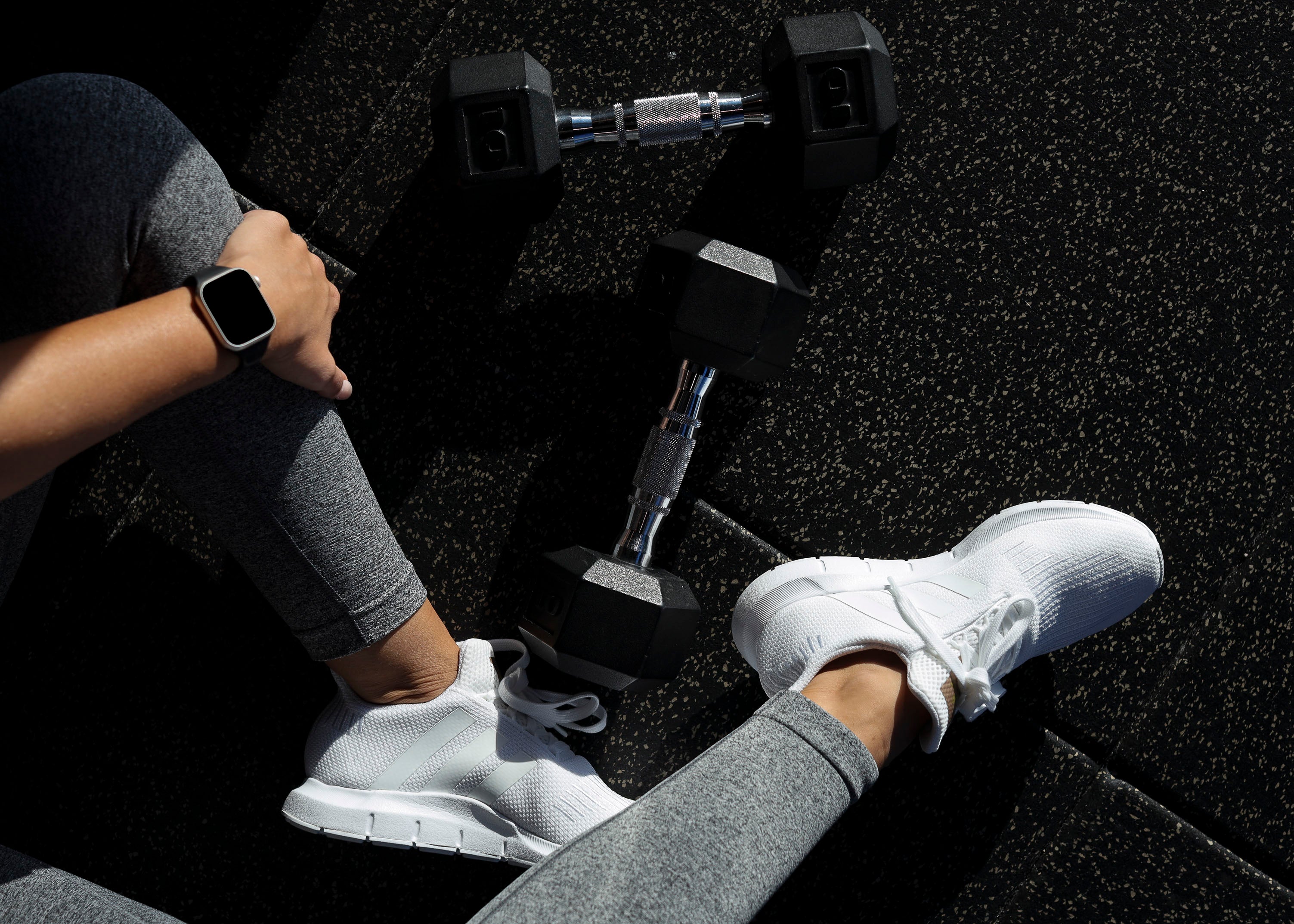 Overhead view of dumbbells and sneakers on a gym floor, with a smartwatch on the wrist