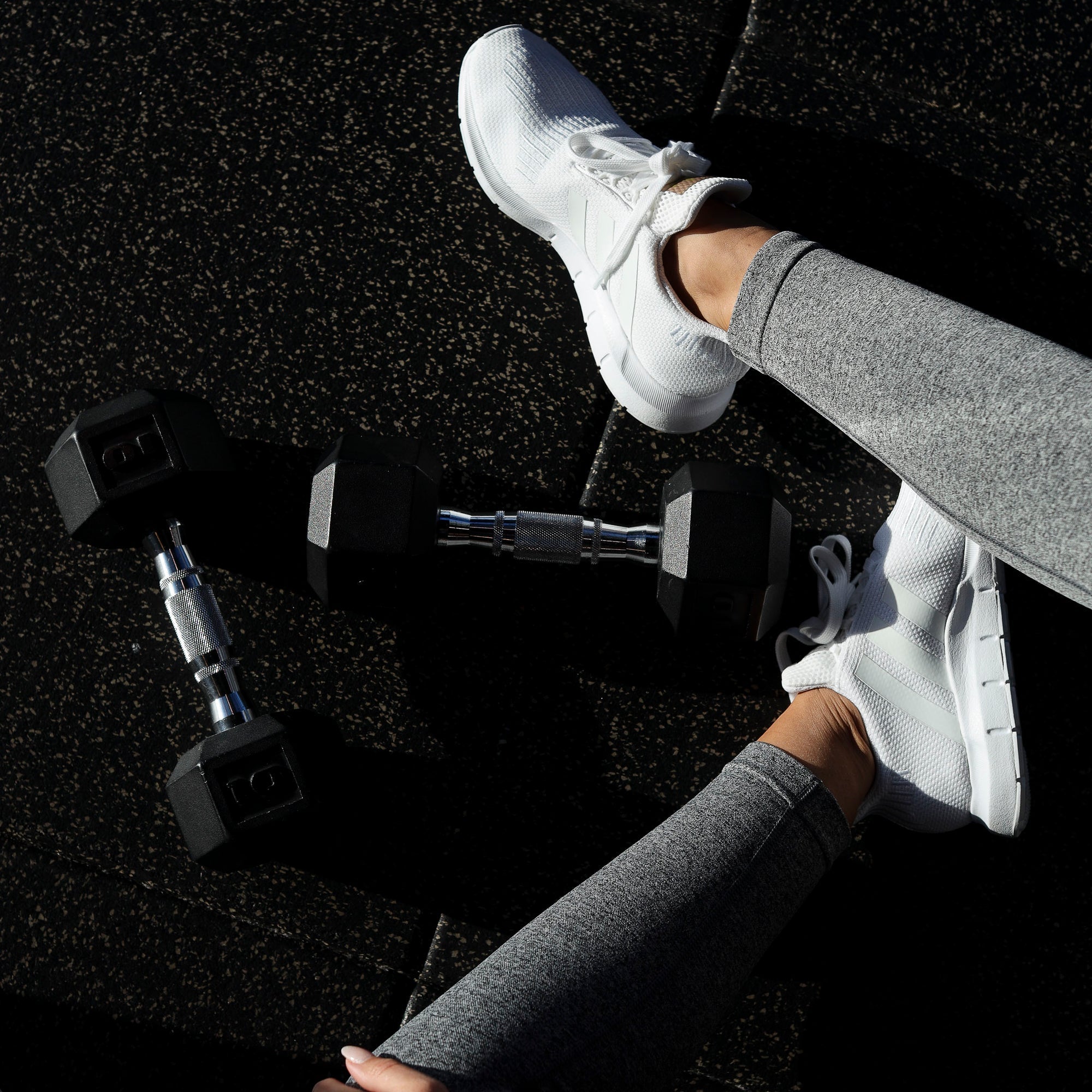 Overhead view of a person in gray leggings stretching on a gym floor beside dumbbells