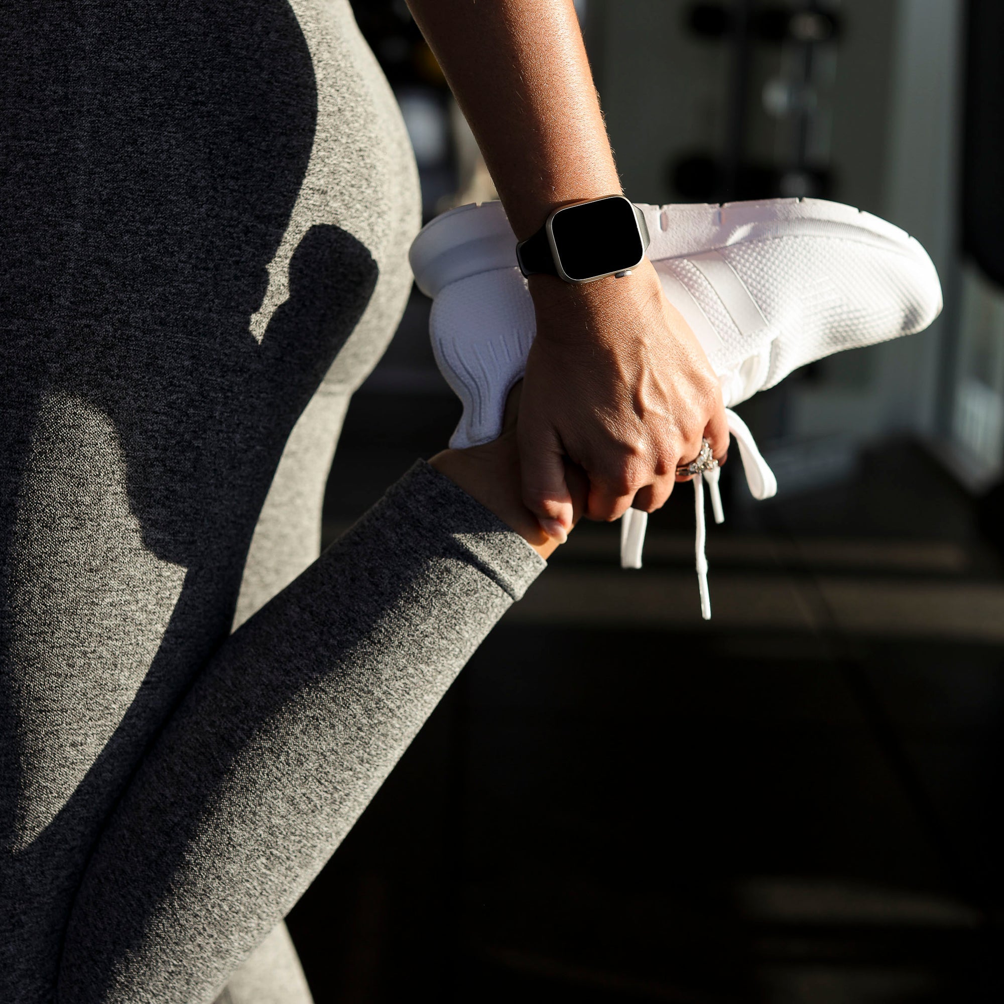 Close-up of a person in gray leggings tying a white sneaker
