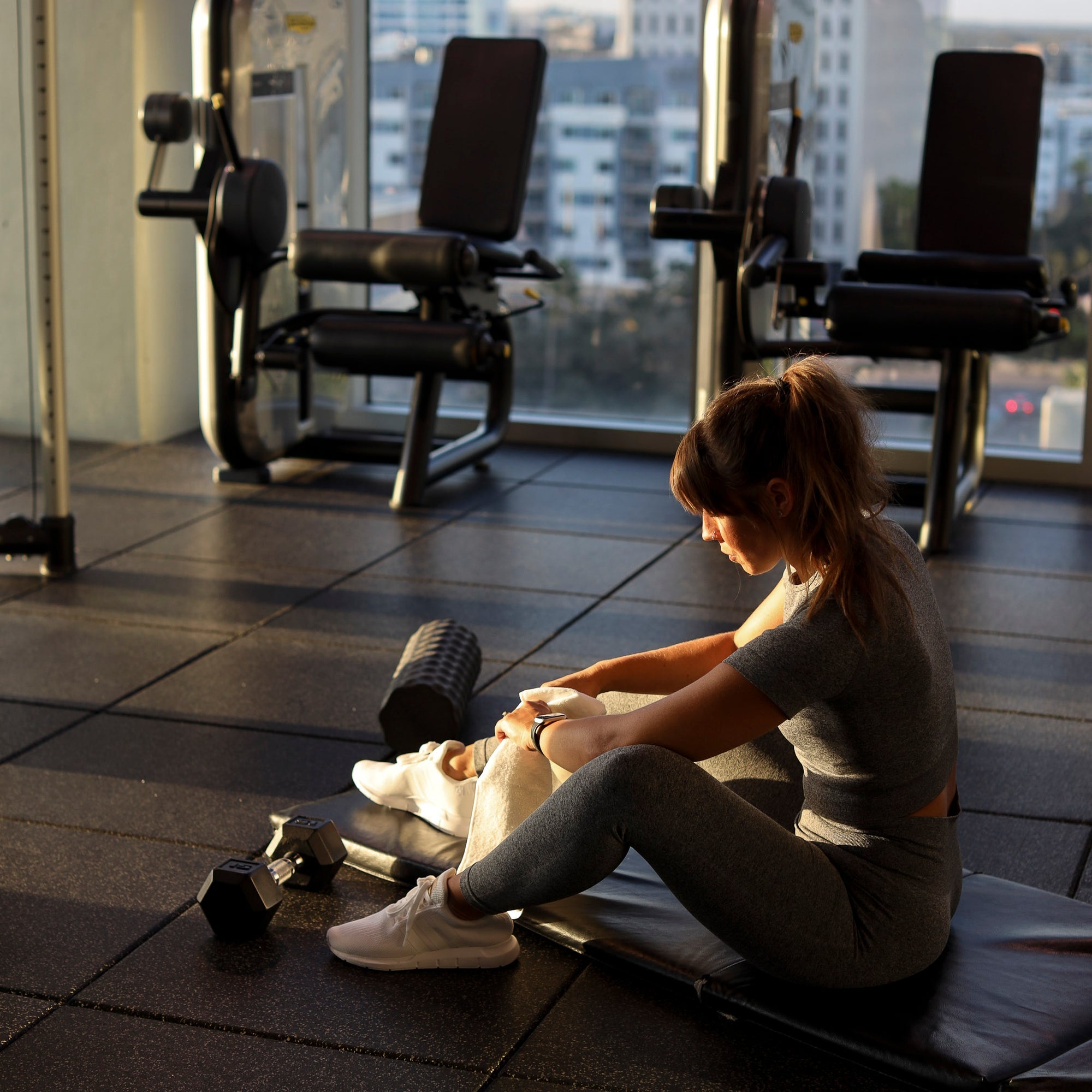Woman sitting on a gym mat stretching beside tall windows