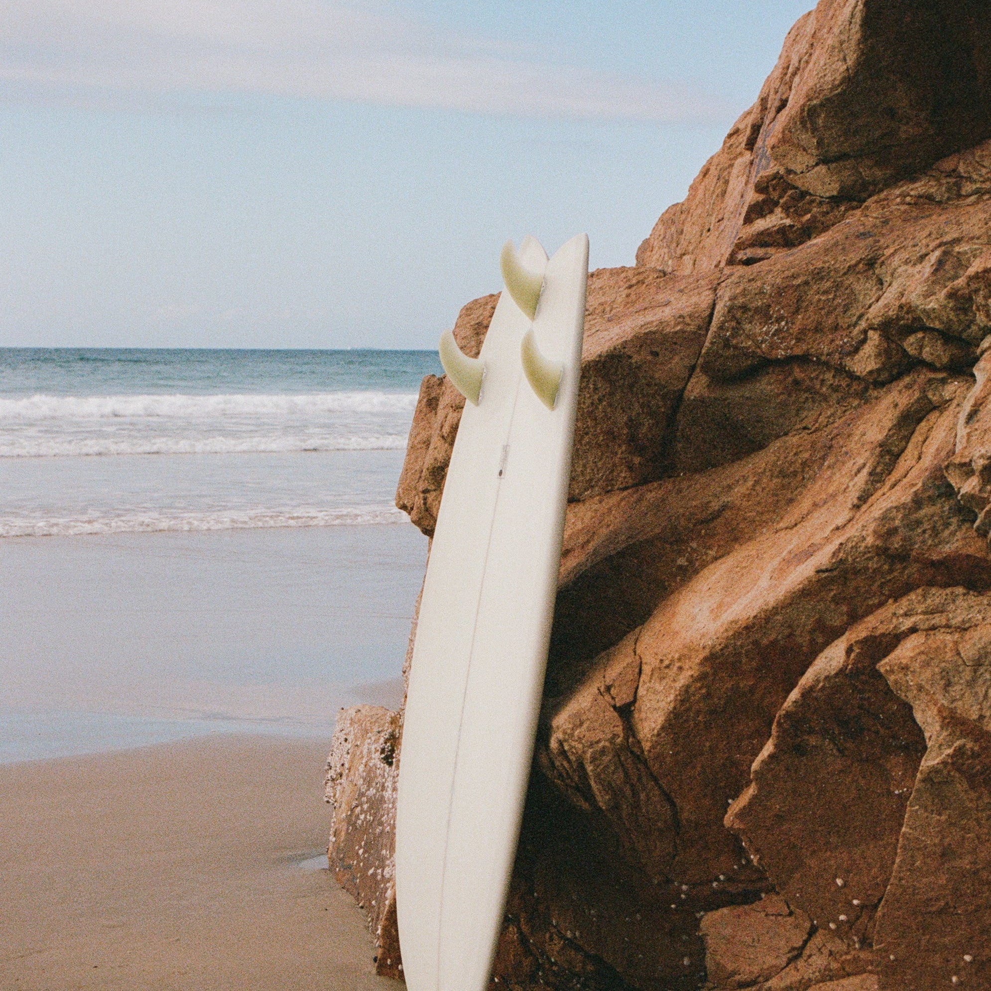 Surfboard leaning against rocks on a sunny beach