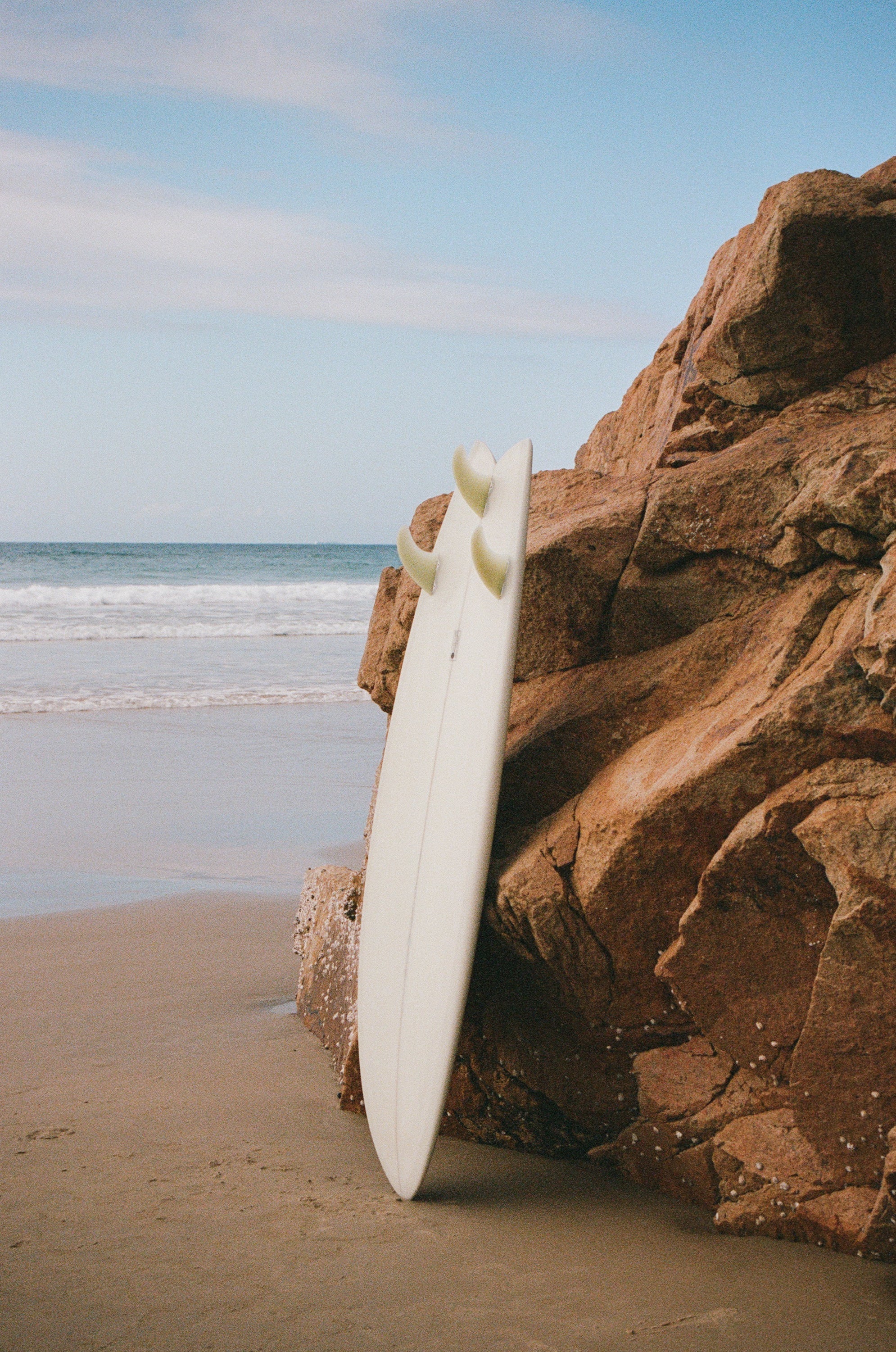 Surfboard leaning against rocks on a sunny beach