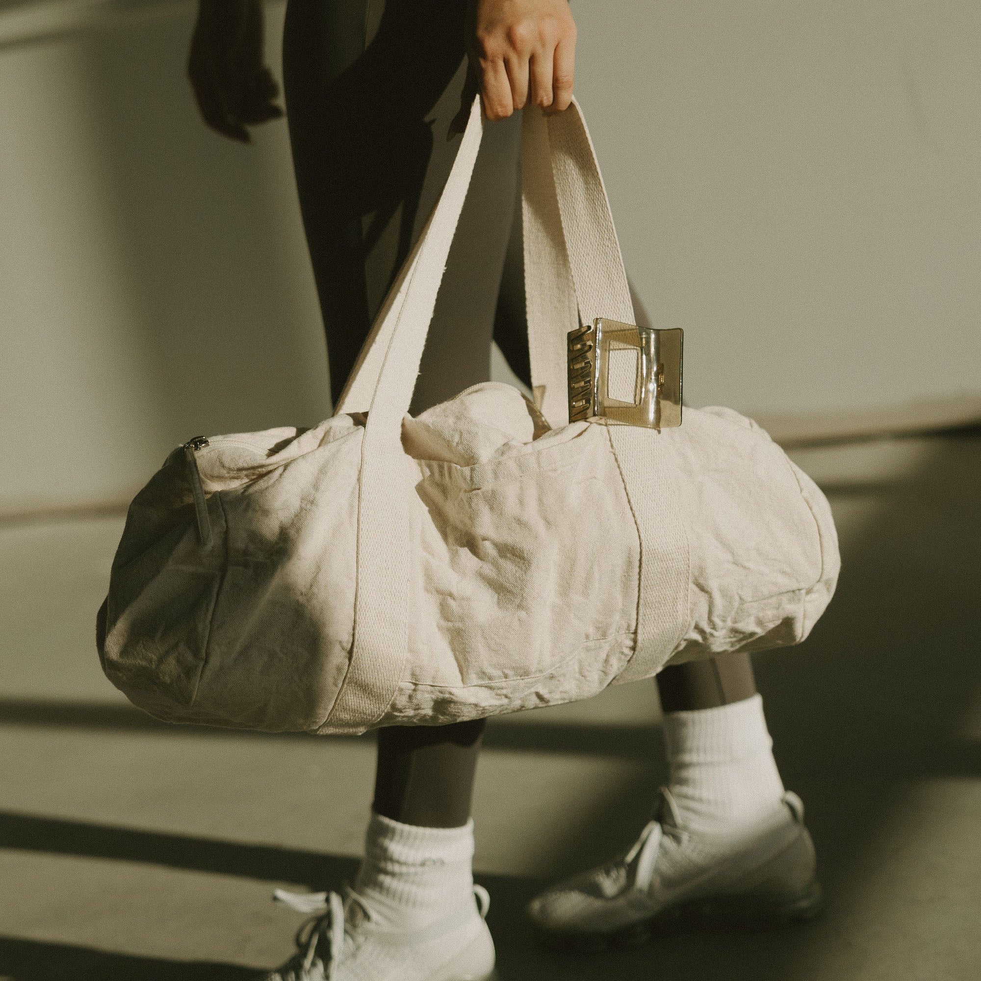 Person carrying a cream duffel bag, wearing white sneakers