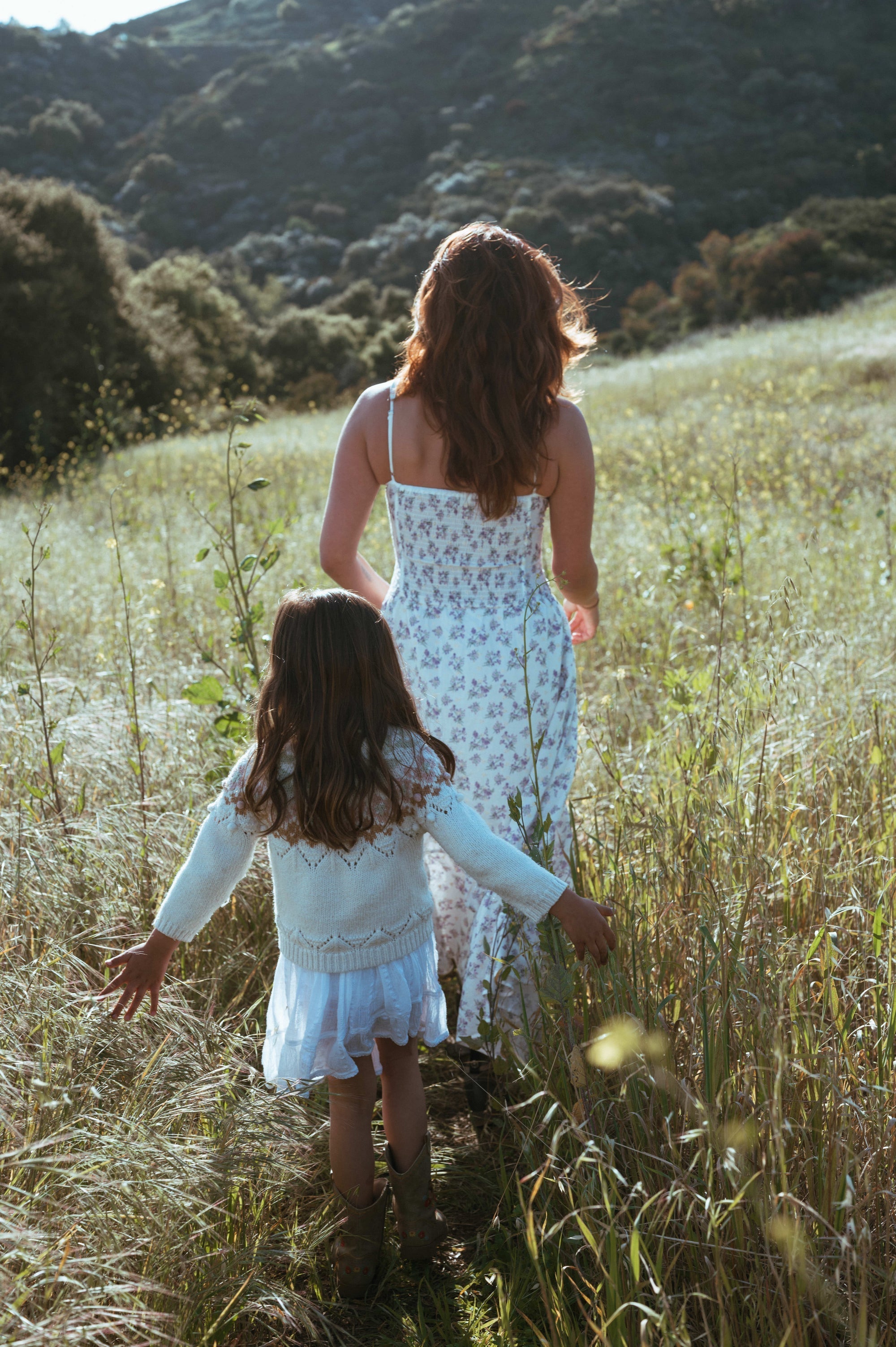 Mother and young daughter walking through a grassy field