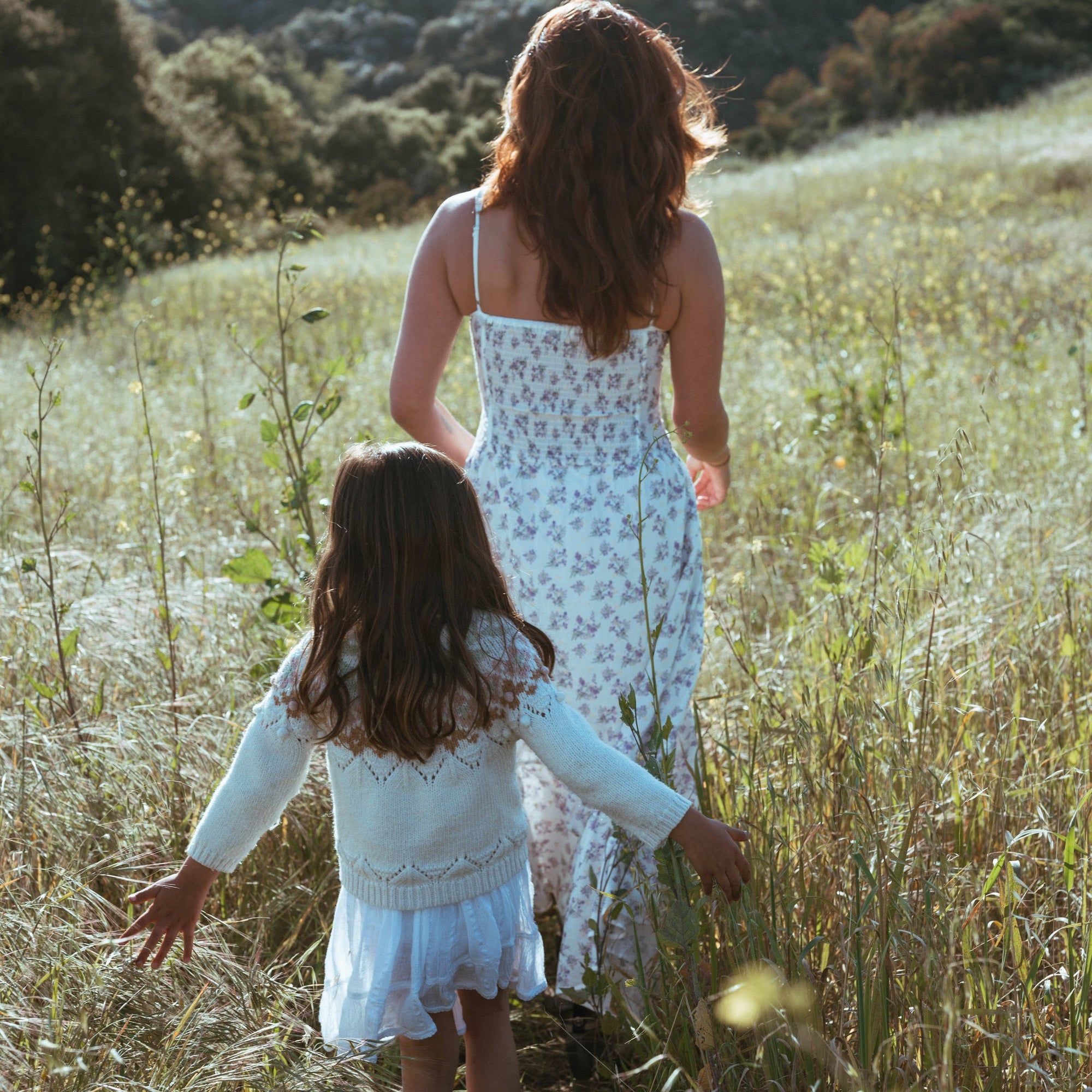 Mother and young daughter walking through a grassy field
