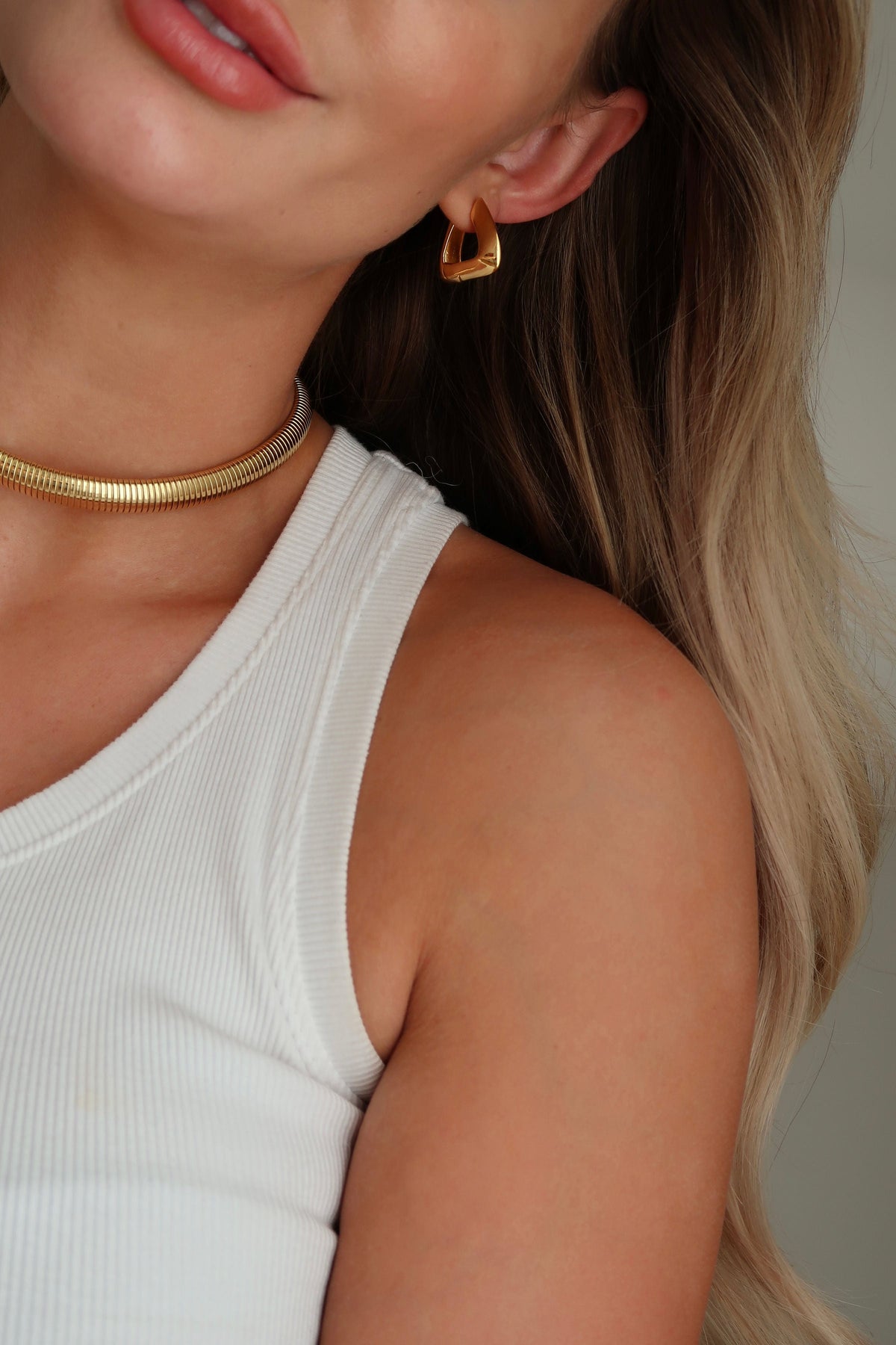Woman with glowing skin and gold jewelry, showcasing healthy hair and radiant skin