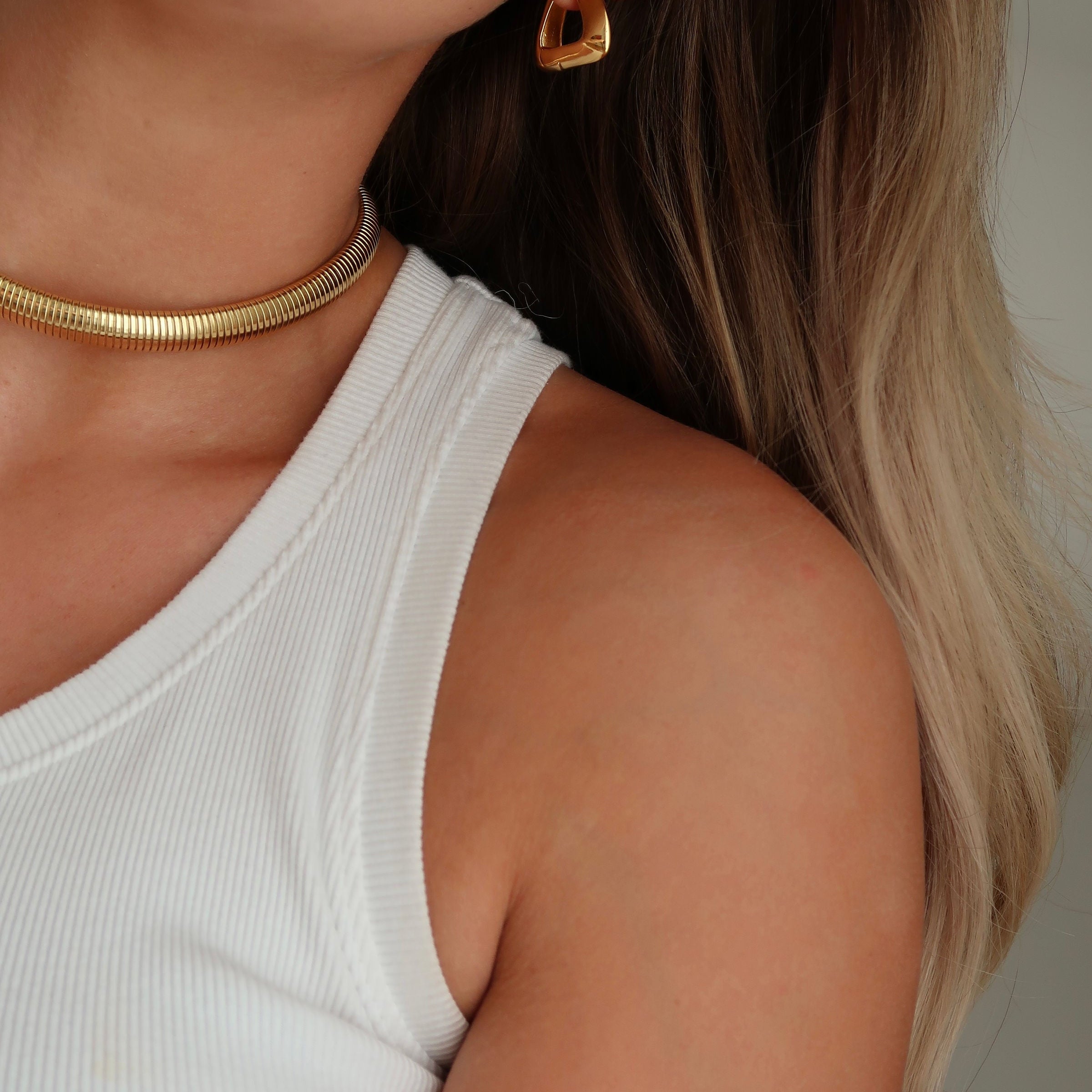 Woman with glowing skin and gold jewelry, showcasing healthy hair and radiant skin