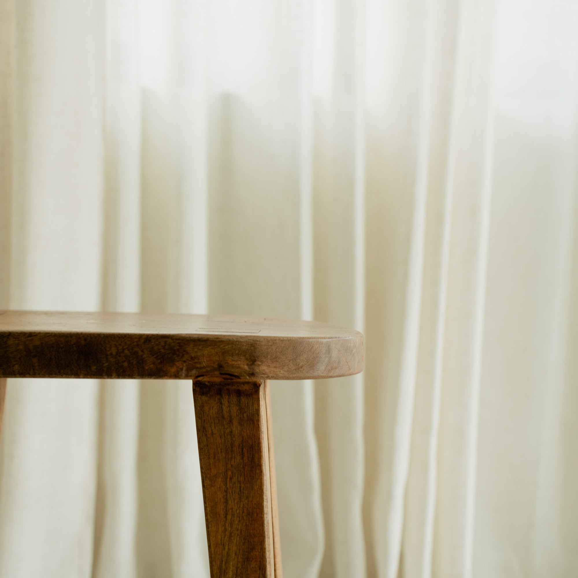 Sheer curtains and a wooden stool beside a sunlit window