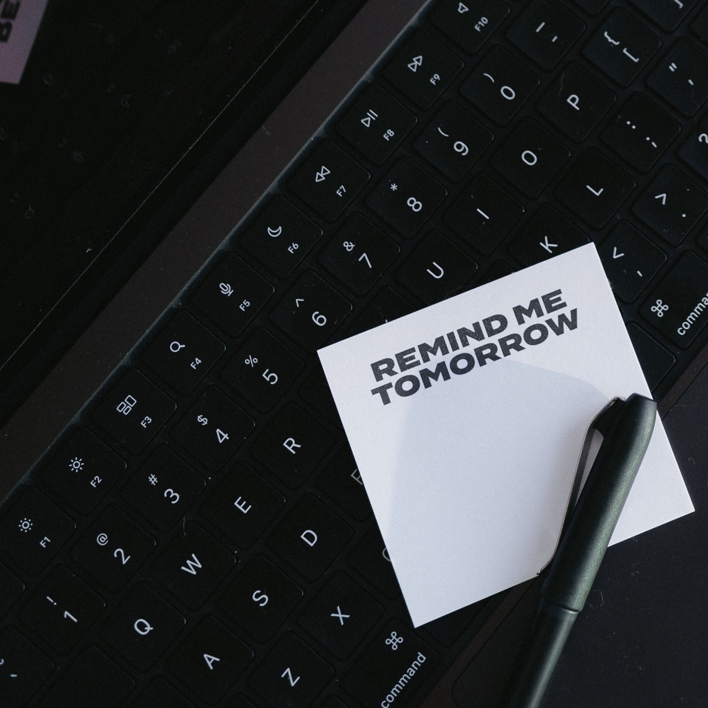 Sticky note reading "Remind me tomorrow" and a pen on a laptop keyboard