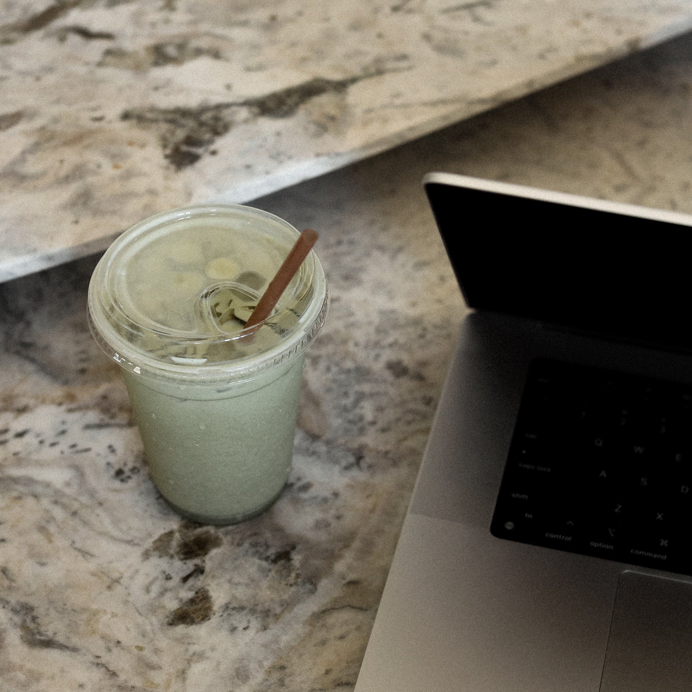 Green smoothie on a kitchen counter next to a laptop