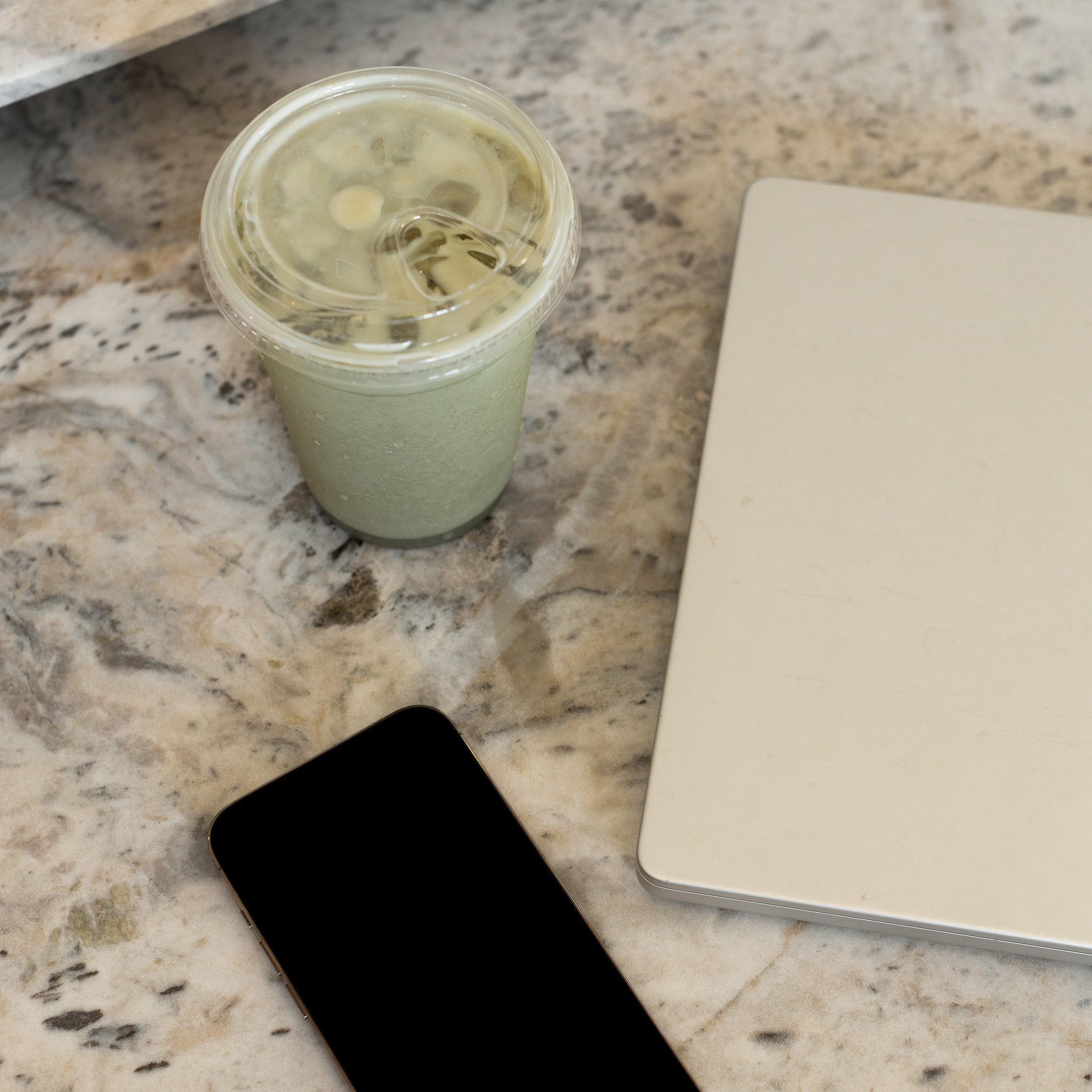 Flat lay of a green smoothie drink, a notebook, and a phone on a marble surface