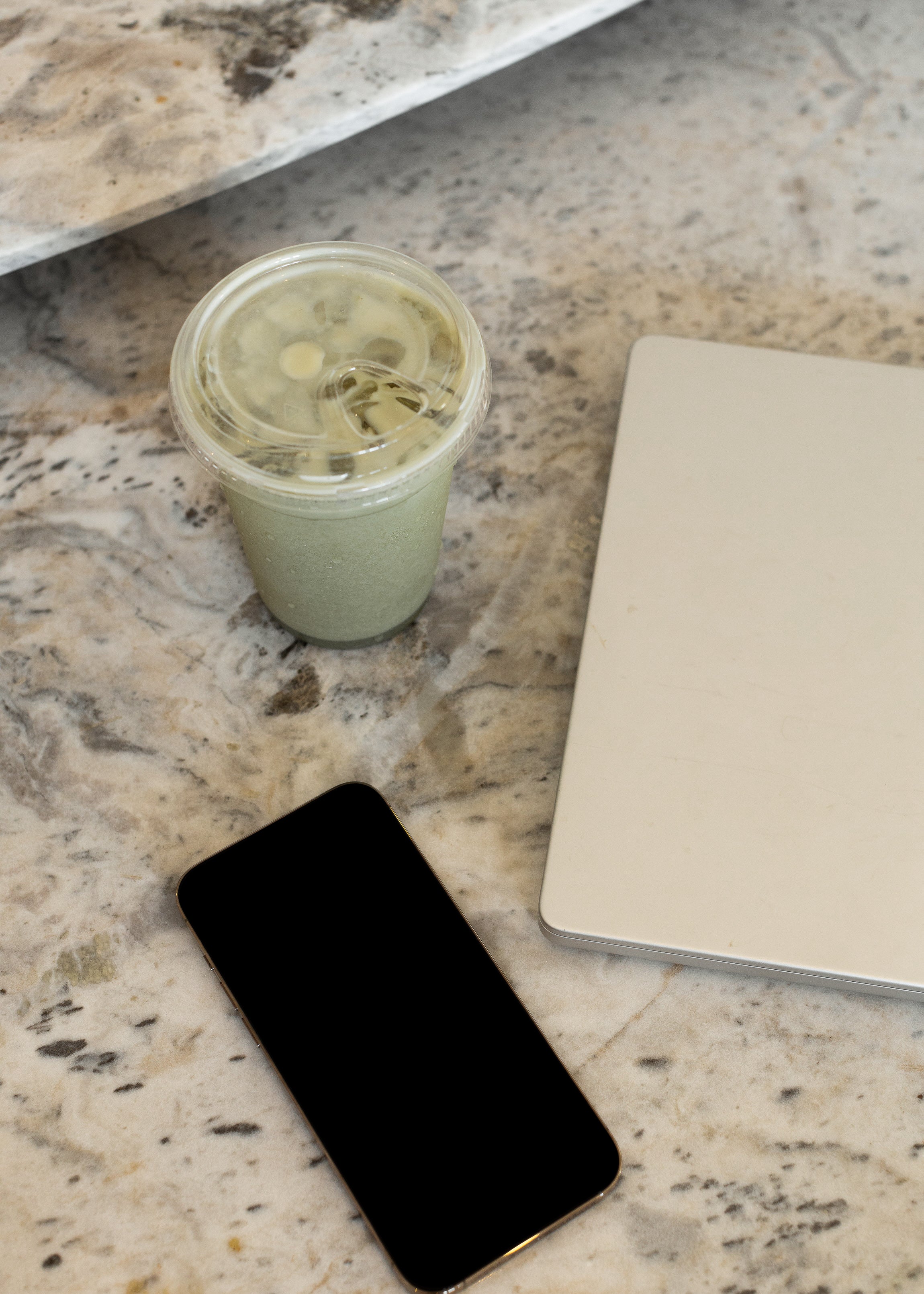 Flat lay of a green smoothie drink, a notebook, and a phone on a marble surface