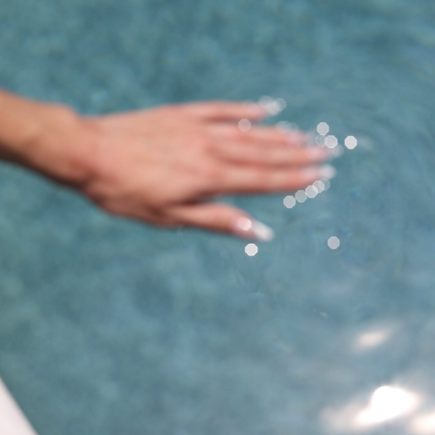 Hand skimming the surface of clear blue water