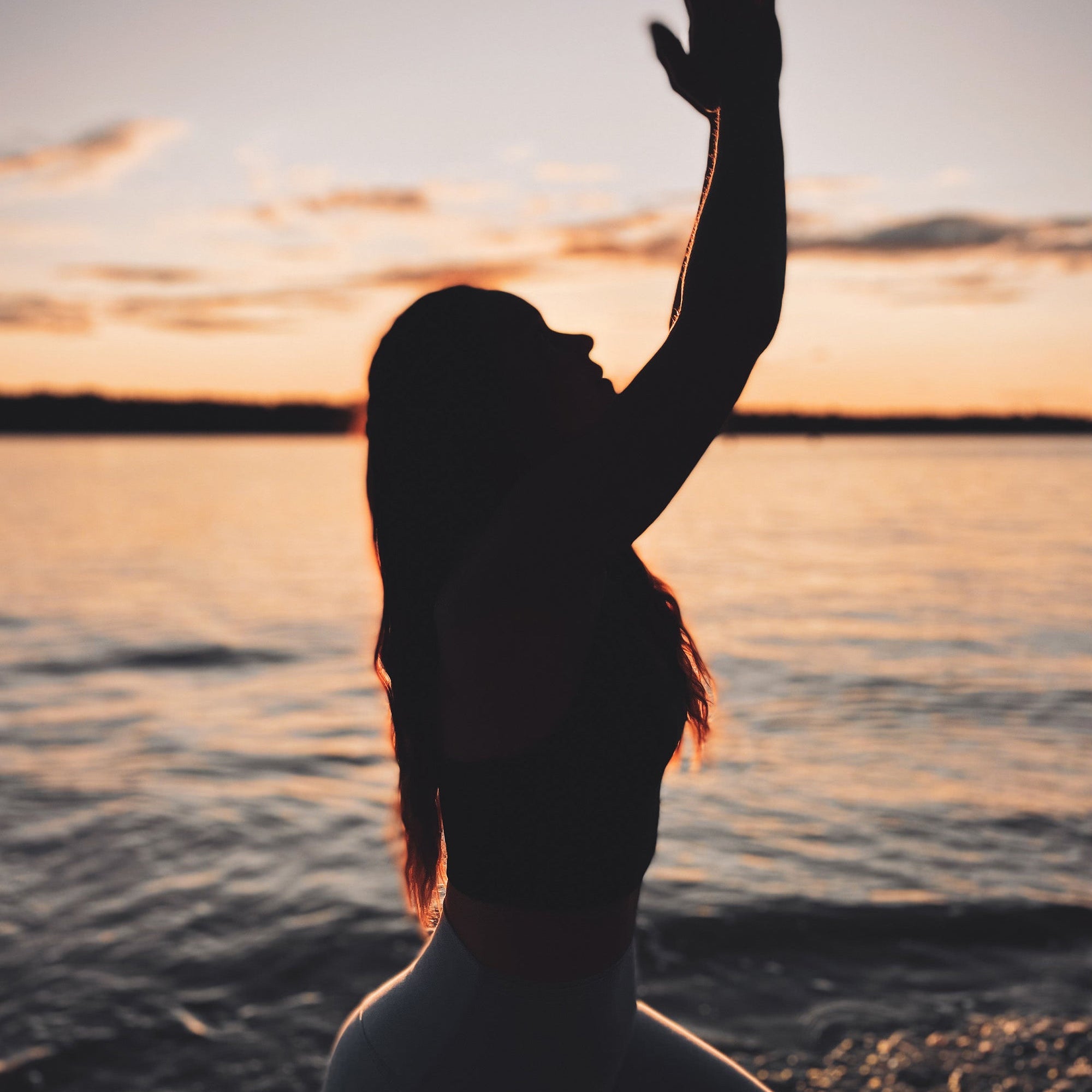 Silhouette of a woman in a yoga lunge beside the water at sunset