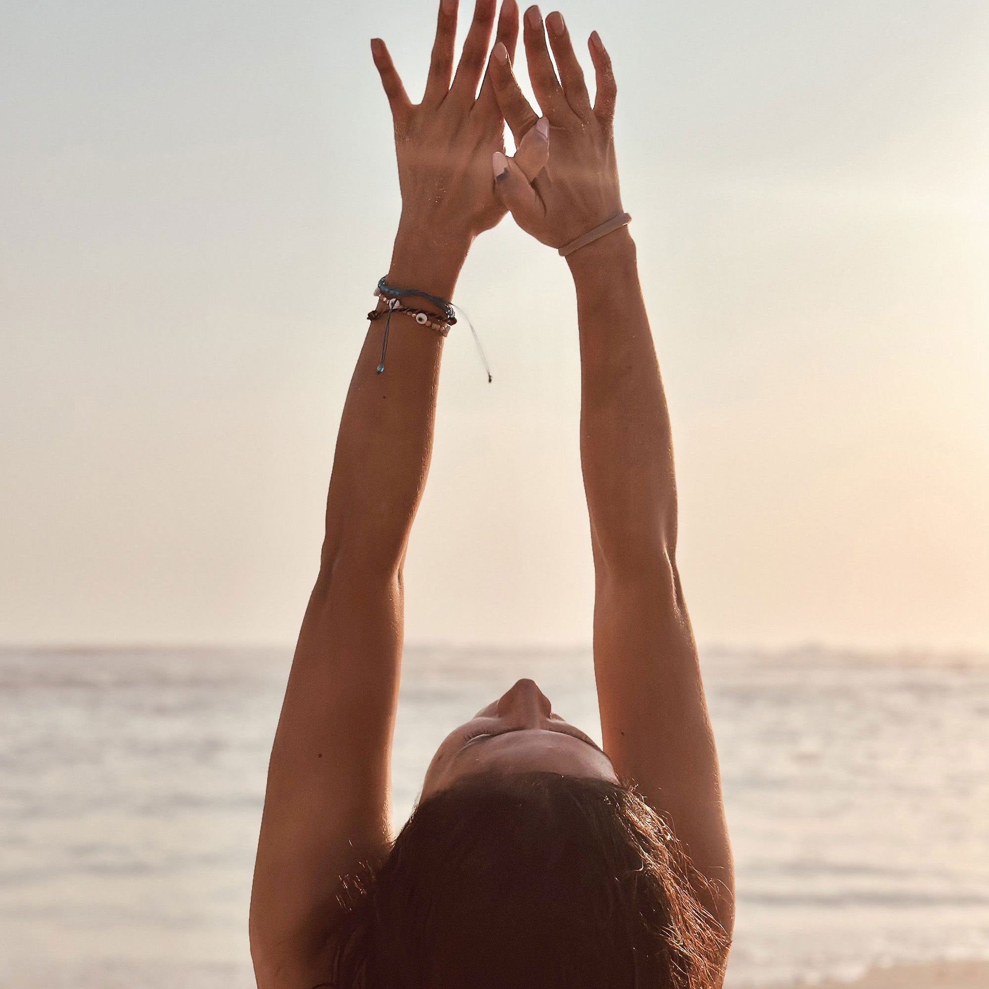 Woman raising her arms overhead on a beach at sunrise