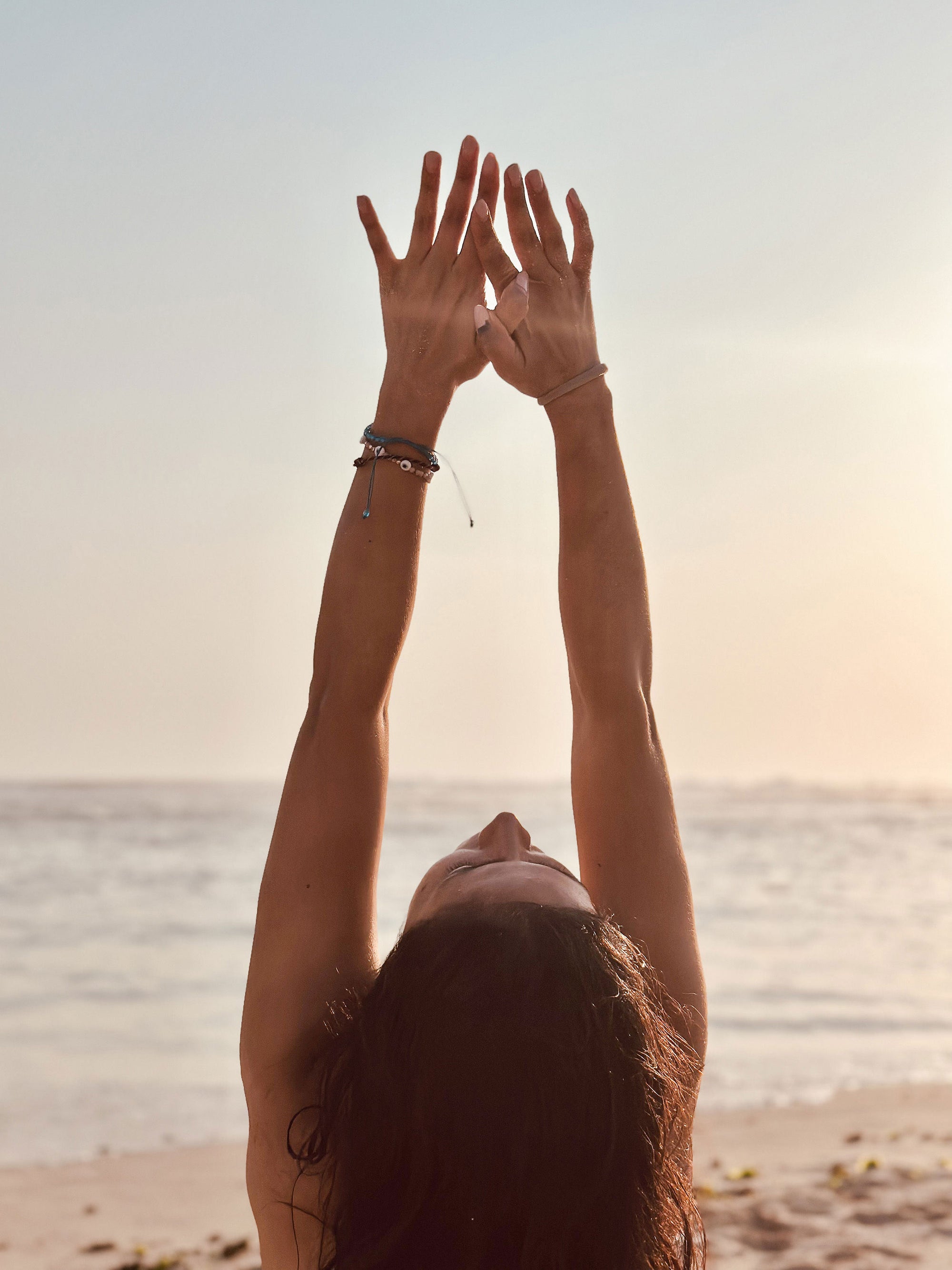 Woman raising her arms overhead on a beach at sunrise
