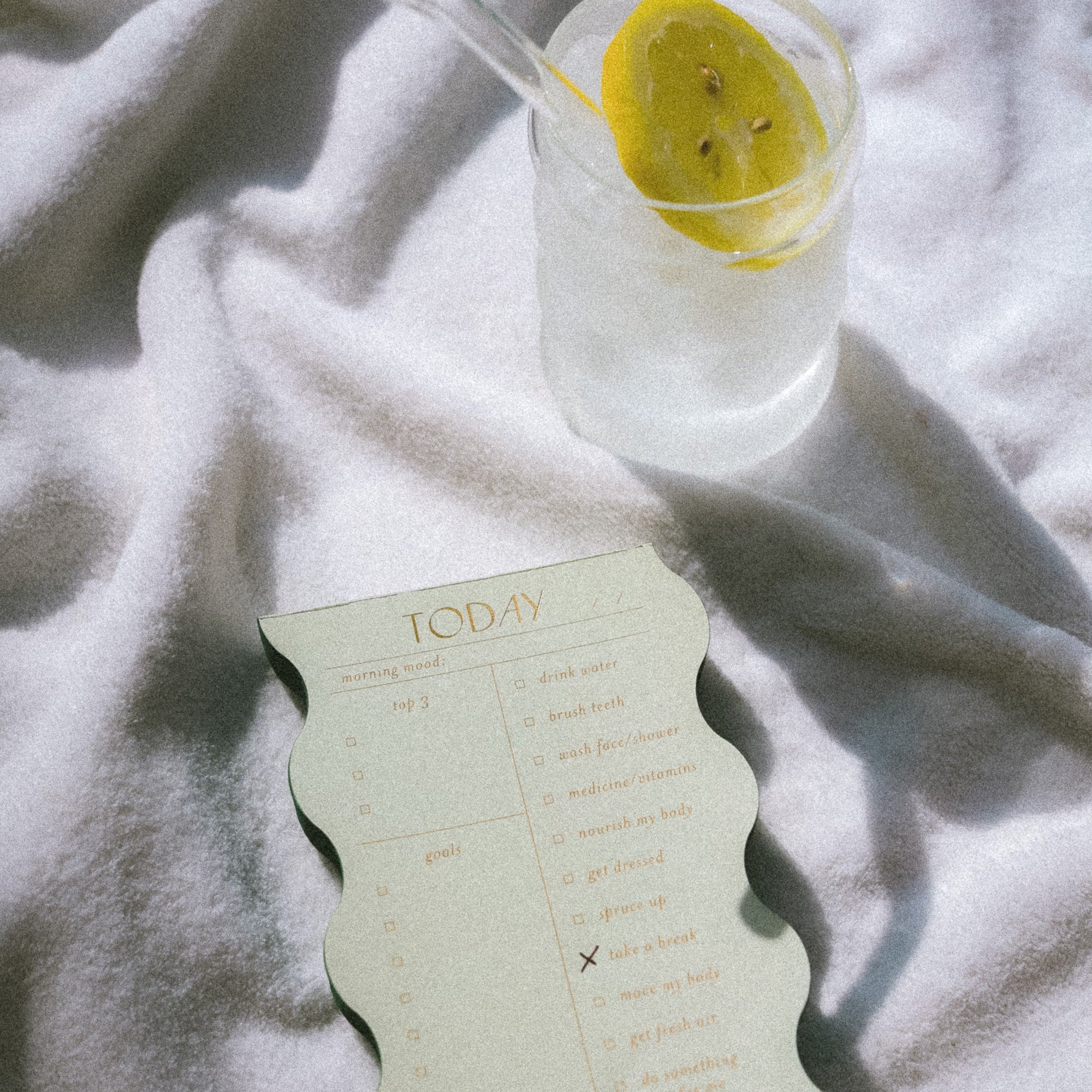 Glass of lemon water and a checklist notepad on a soft gray blanket