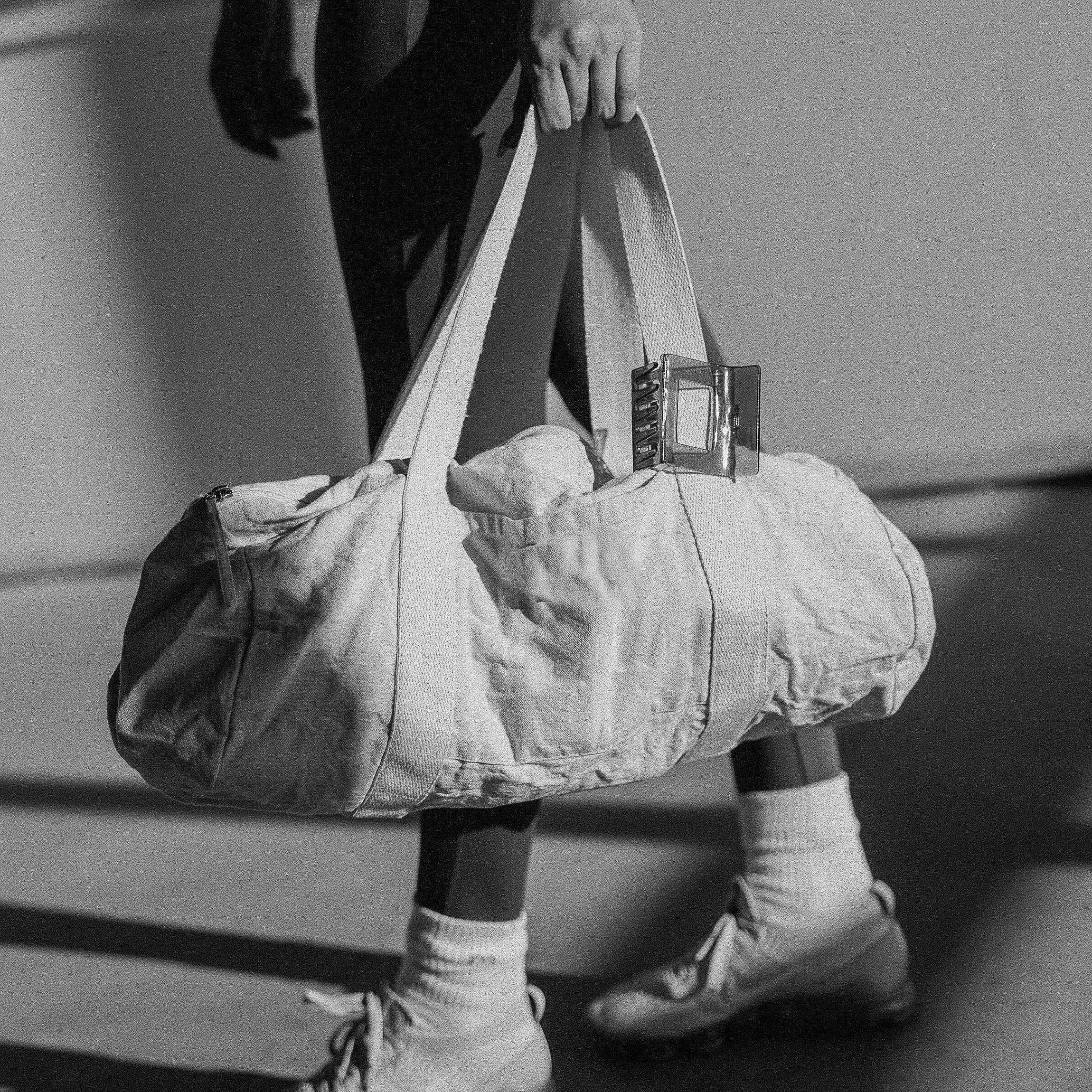 Person walking with a gym duffel bag, black and white