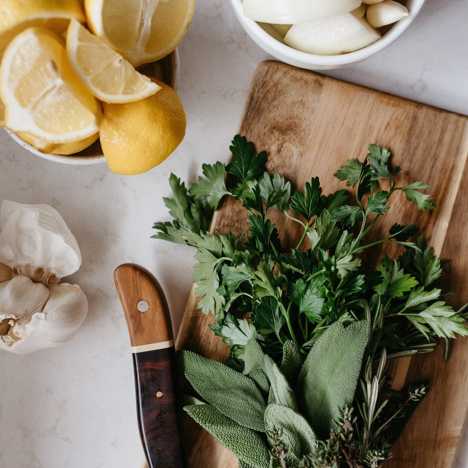 Fresh herbs, lemon wedges and garlic on a wooden cutting board
