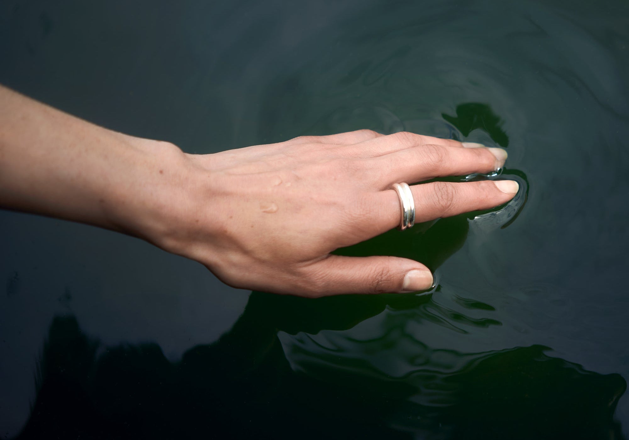 Hand touching the surface of dark, still water