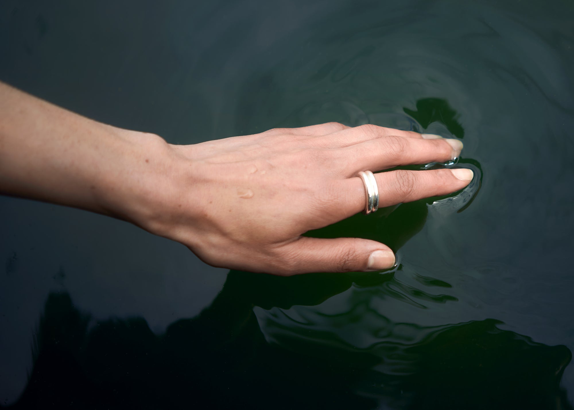 Hand touching the surface of dark, still water
