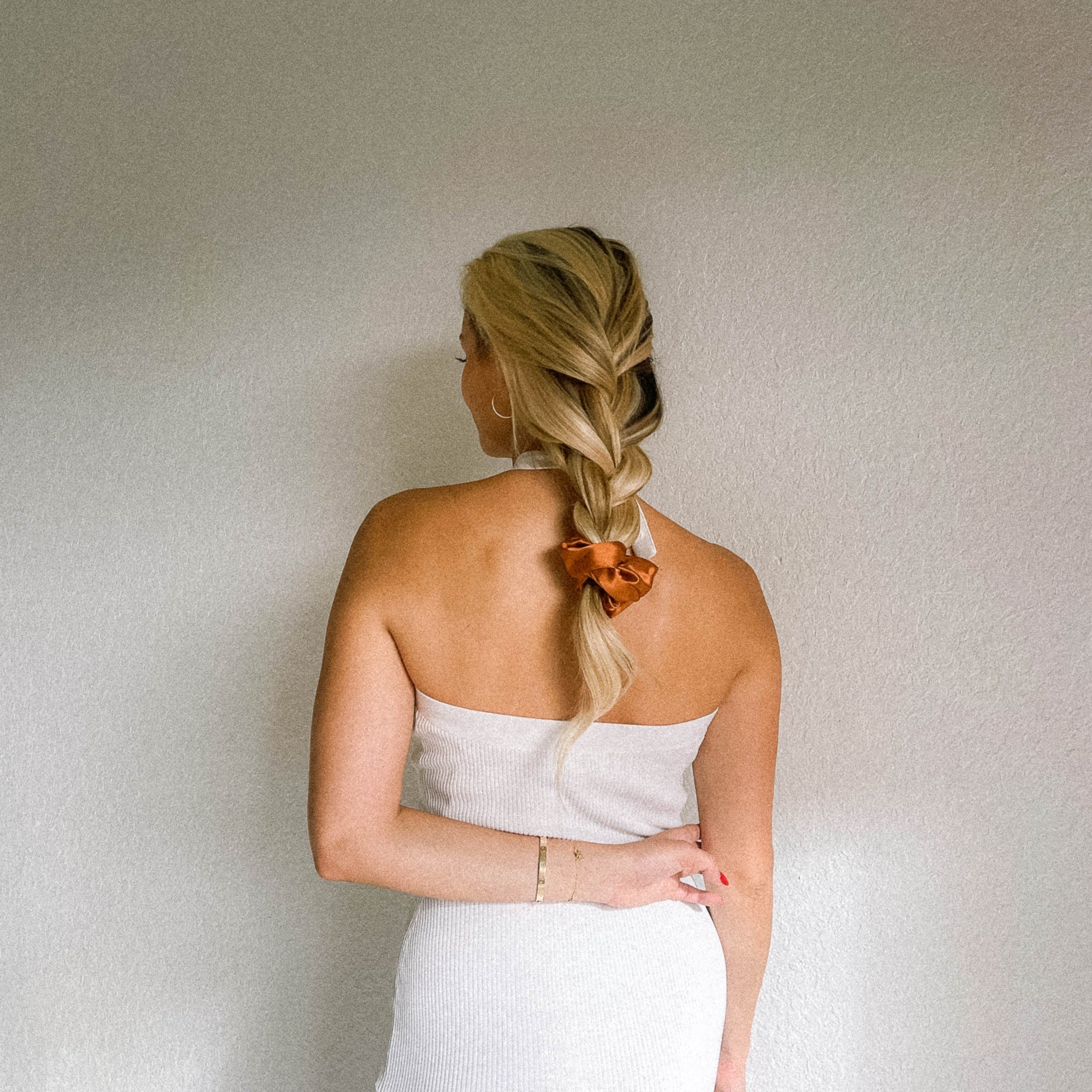 Woman seen from behind with a long braid tied with an orange scrunchie