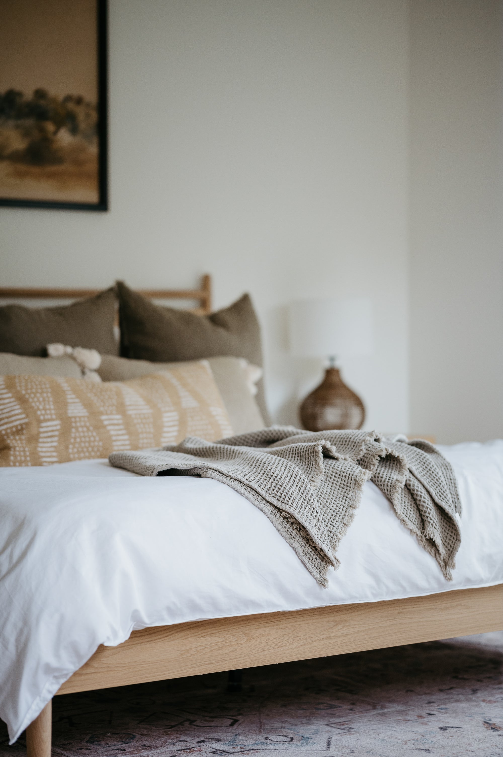 Neatly made bed with white linens and neutral pillows