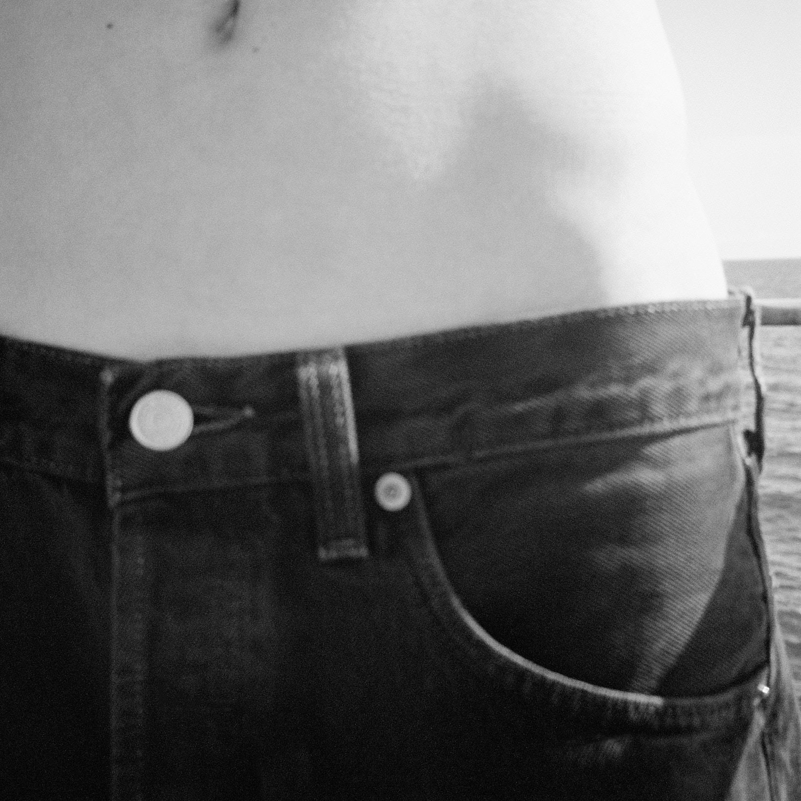 Black-and-white close-up of a bare midriff above black jeans