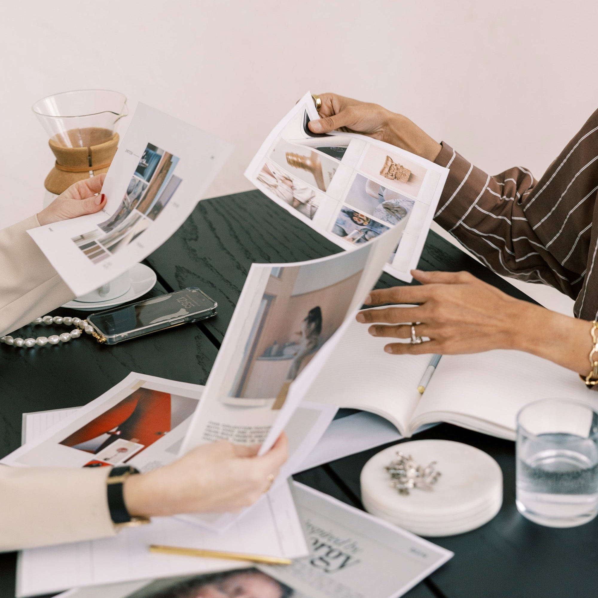 Hands leafing through magazines and photo prints on a table