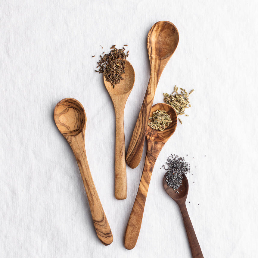 Wooden spoons holding dried herbs and spices on a white surface