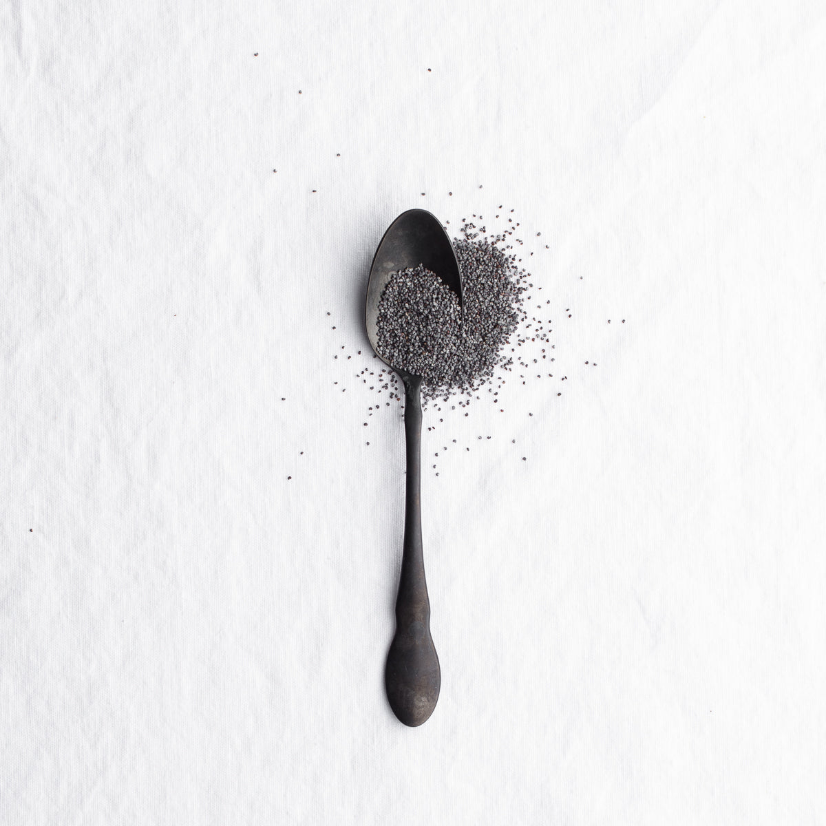 Black spoon spilling tiny dark seeds on a white surface