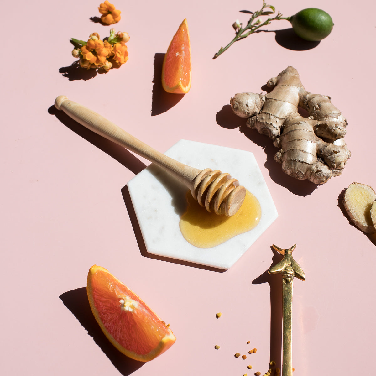 Honey dipper, ginger root and orange wedges on a pink surface