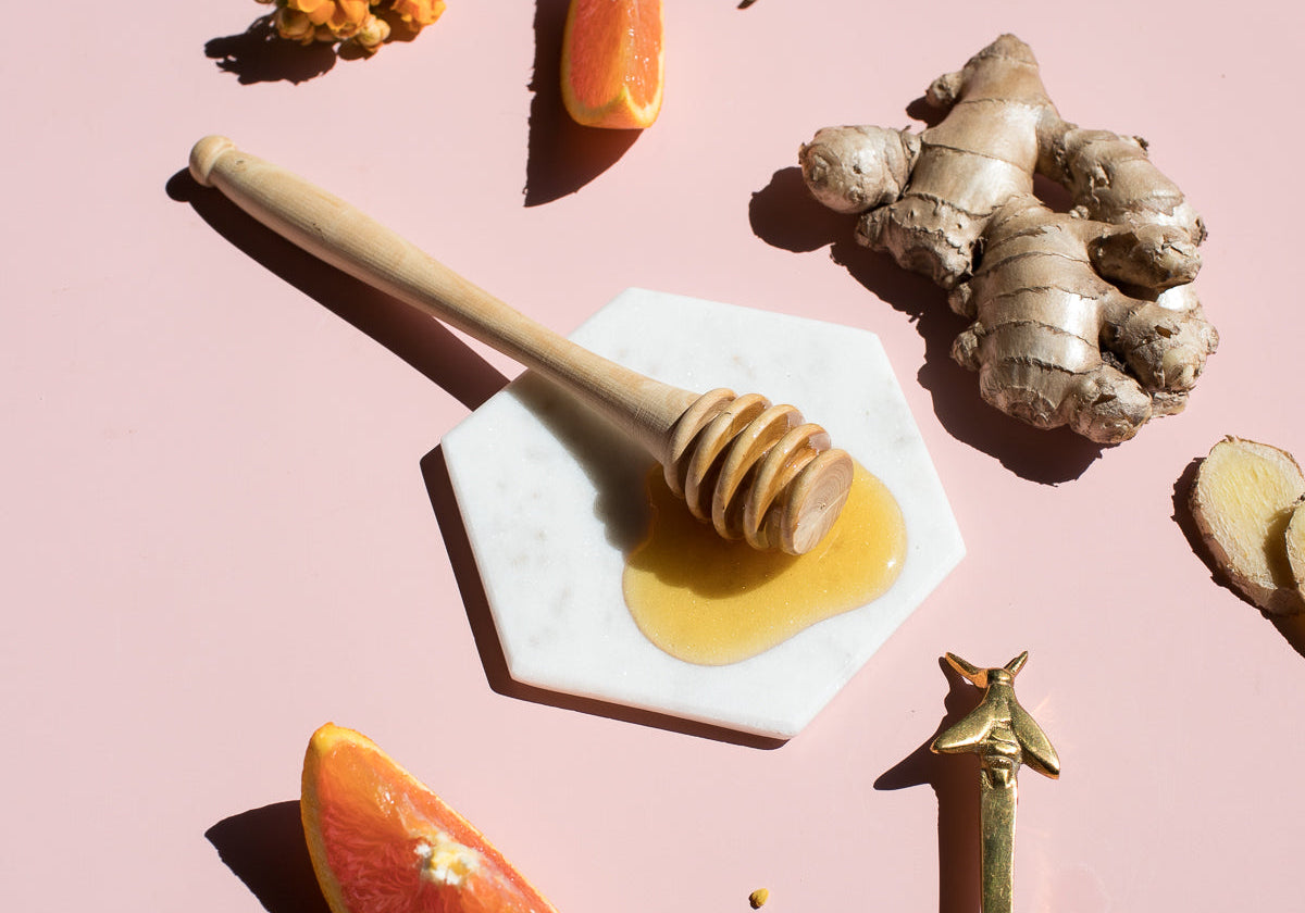 Honey dipper, ginger root and orange wedges on a pink surface