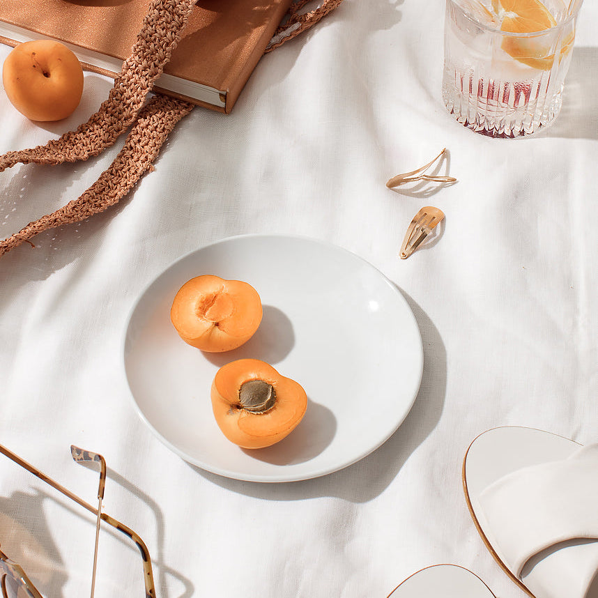 Halved apricots on a plate beside sunglasses and an iced drink
