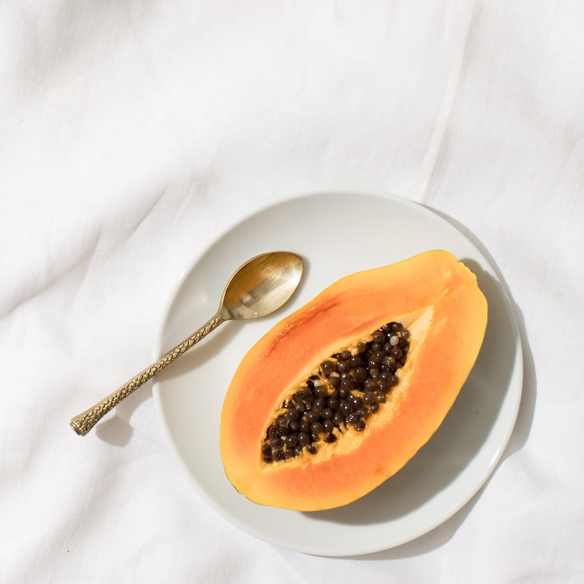 Halved papaya on a plate with a gold spoon