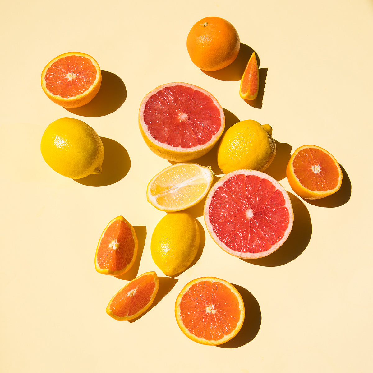 Halved grapefruit, oranges and lemons on a pale yellow surface