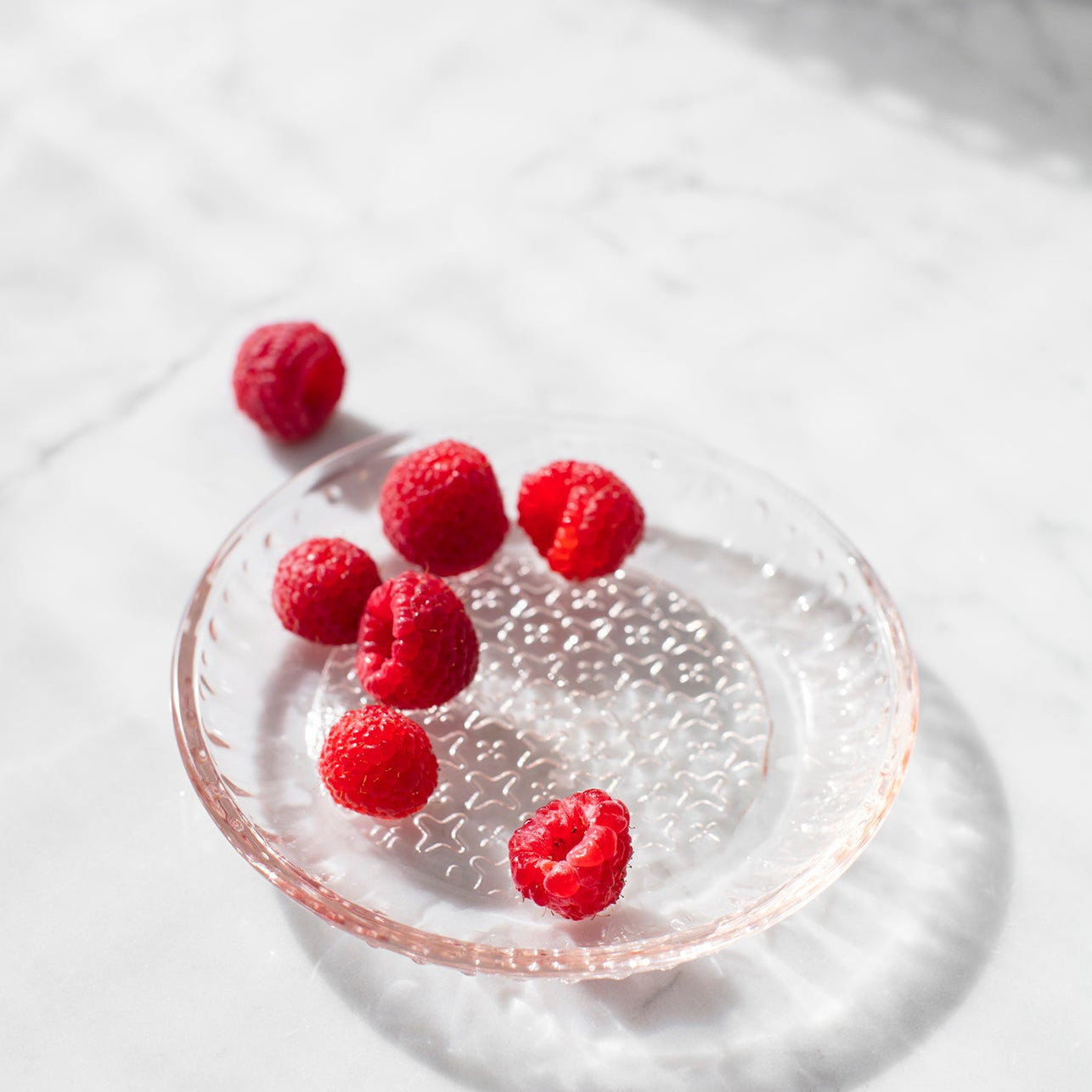 Raspberries on a glass plate in bright light