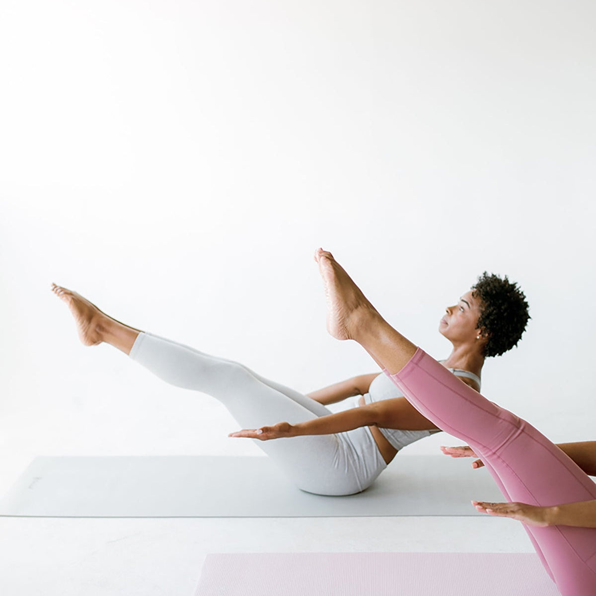 Two people holding a boat pose on exercise mats