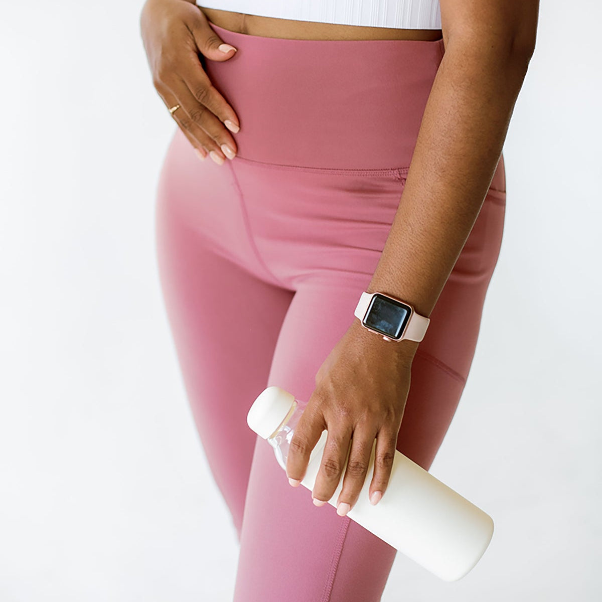 Woman in pink leggings holding a water bottle against her hip, representing staying hydrated for digestion