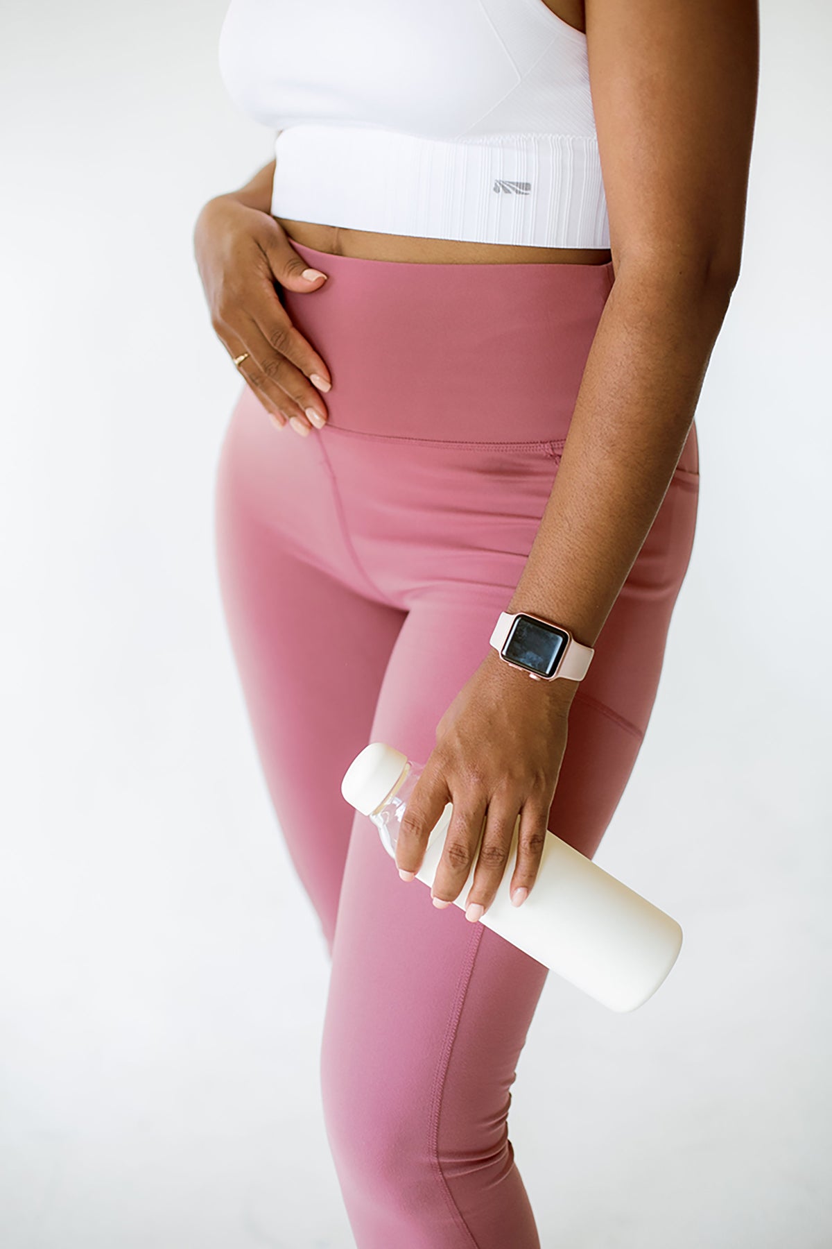 Woman in pink leggings holding a water bottle against her hip, representing staying hydrated for digestion