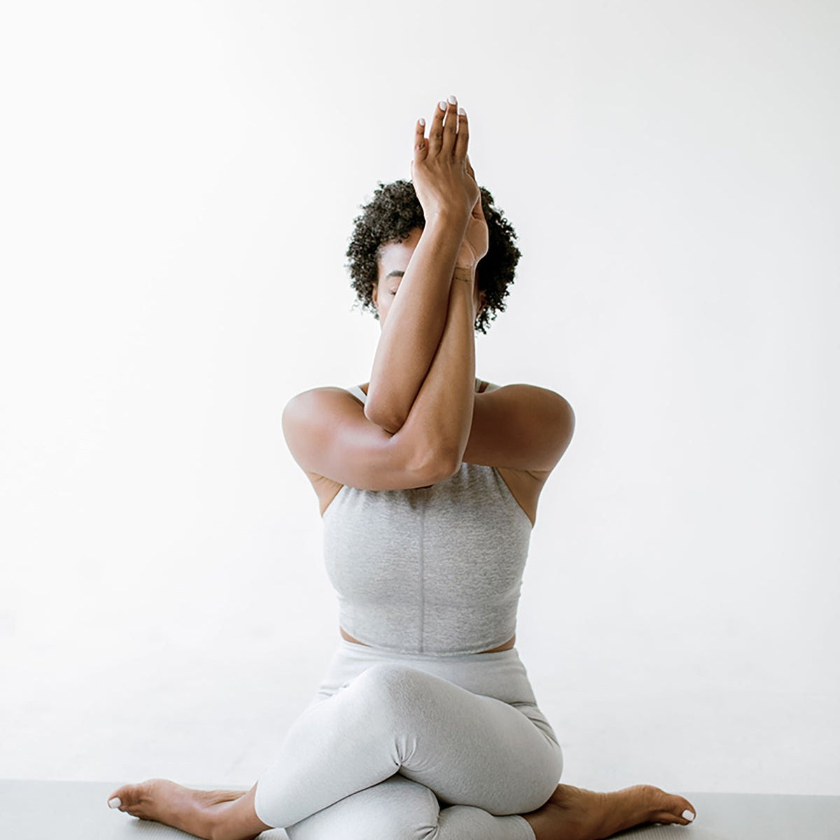Woman seated on a mat in a twisted-arm yoga pose