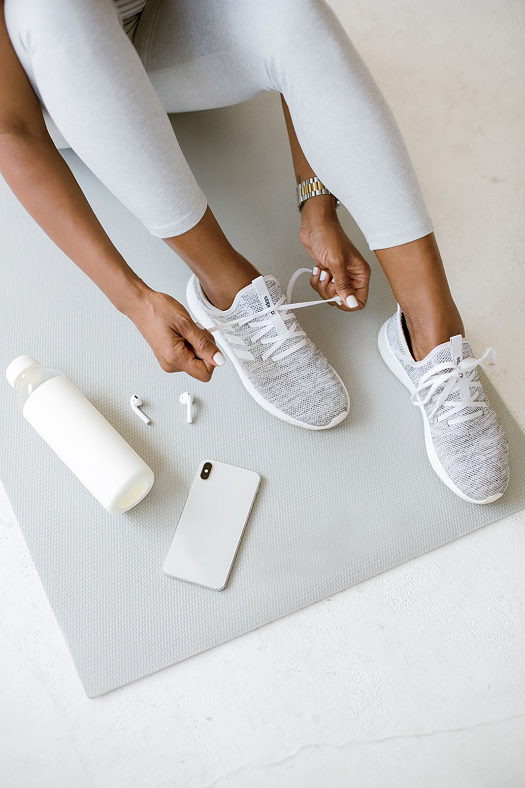 Overhead view of a woman tying her running shoes on a yoga mat, with a water bottle and phone beside her